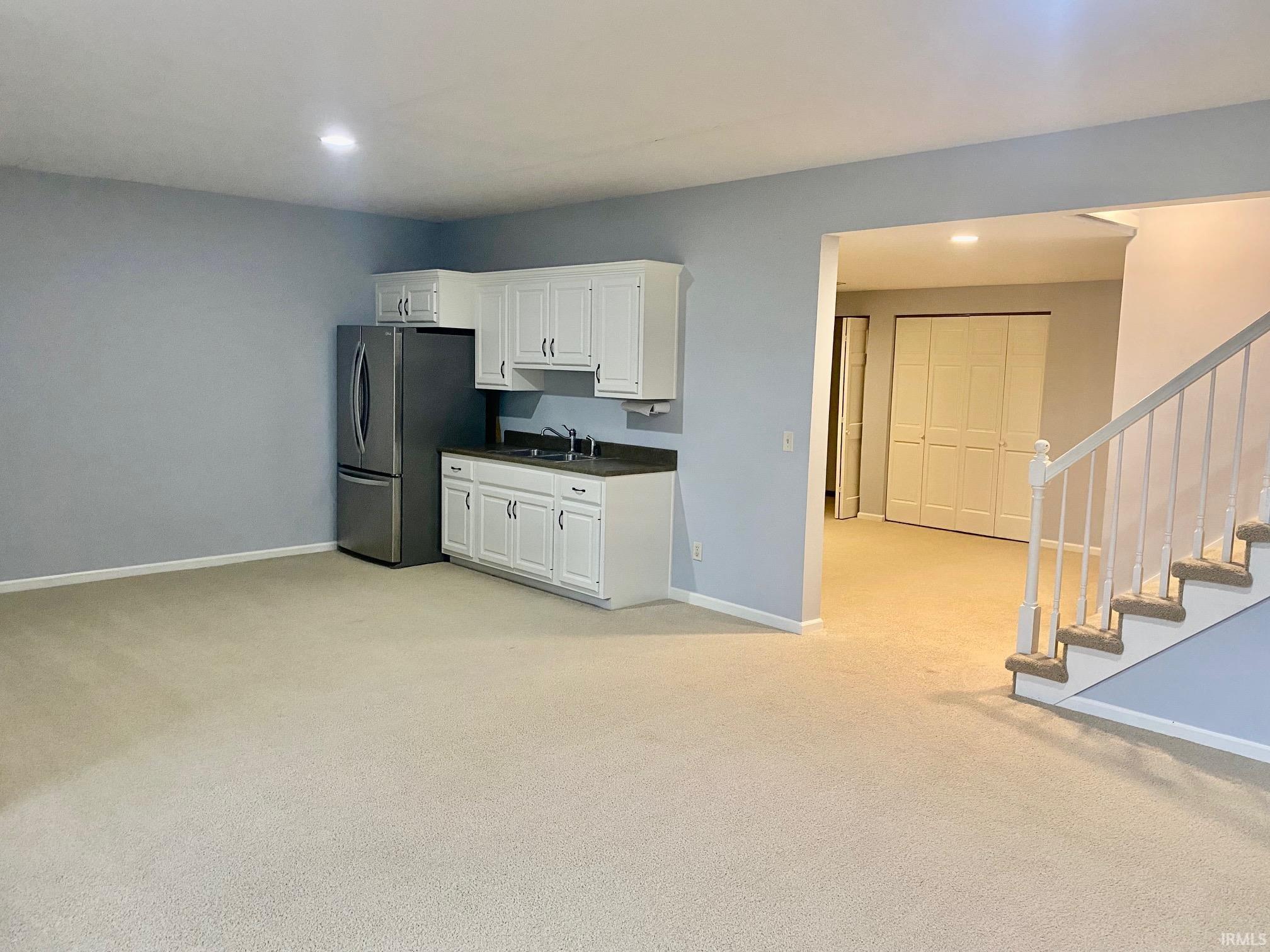Kitchen with dark countertops, light colored carpet, white cabinets, freestanding refrigerator, and recessed lighting