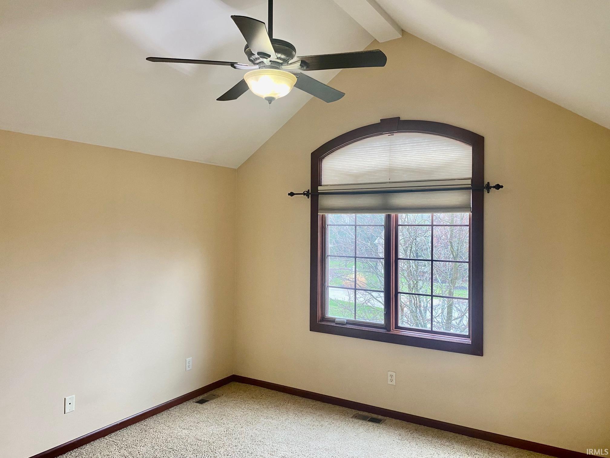 Empty room featuring a ceiling fan, light colored carpet, and beamed ceiling
