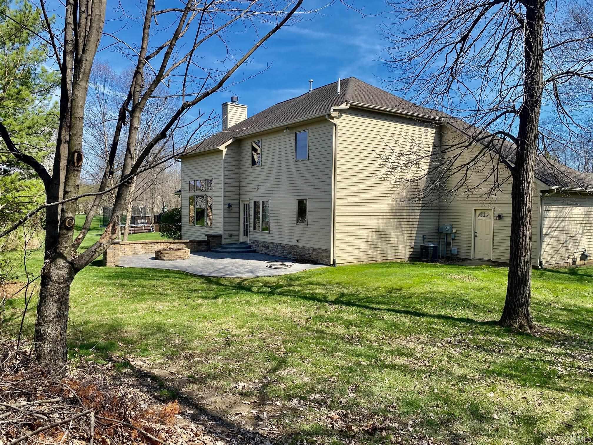 Rear view of property featuring a patio, a lawn, a chimney, and roof with shingles