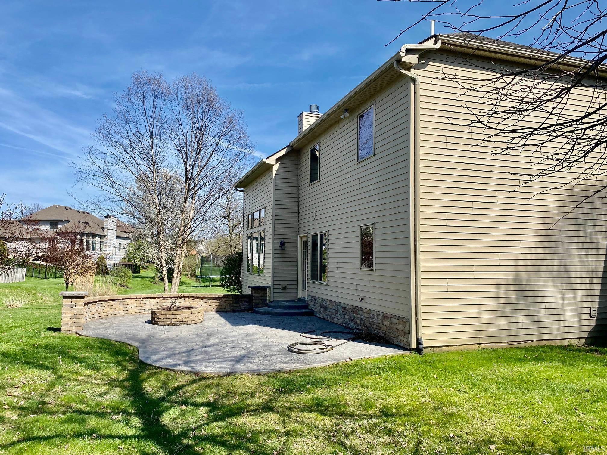 View of side of property featuring a patio, a lawn, a chimney, and an outdoor fire pit
