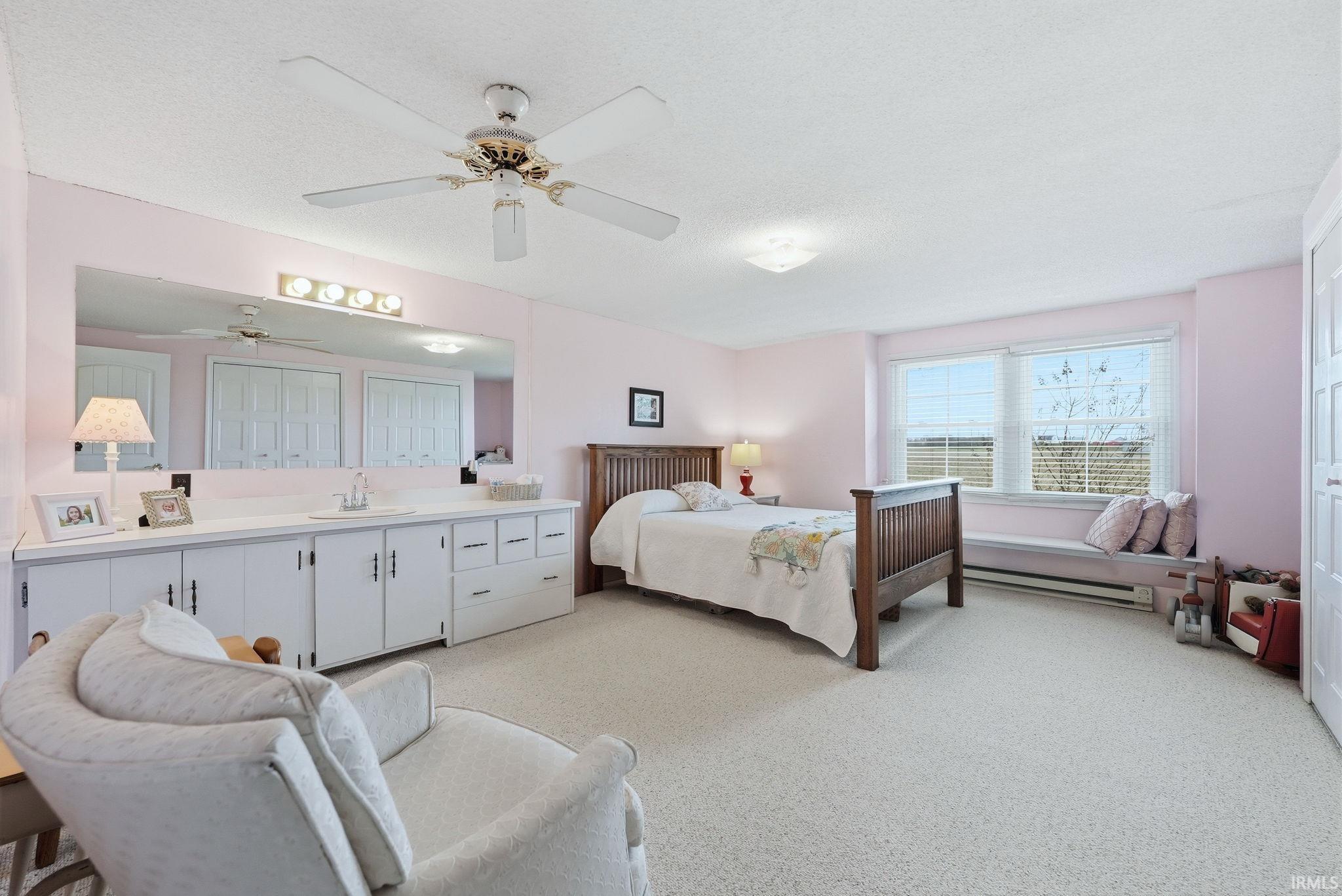 Bedroom featuring a baseboard heating unit, light carpet, ceiling fan, and a textured ceiling