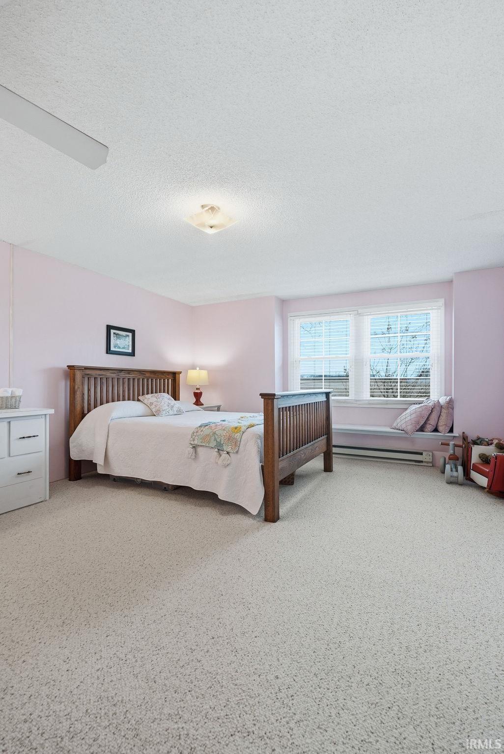 Bedroom featuring a textured ceiling, baseboard heating, and light colored carpet
