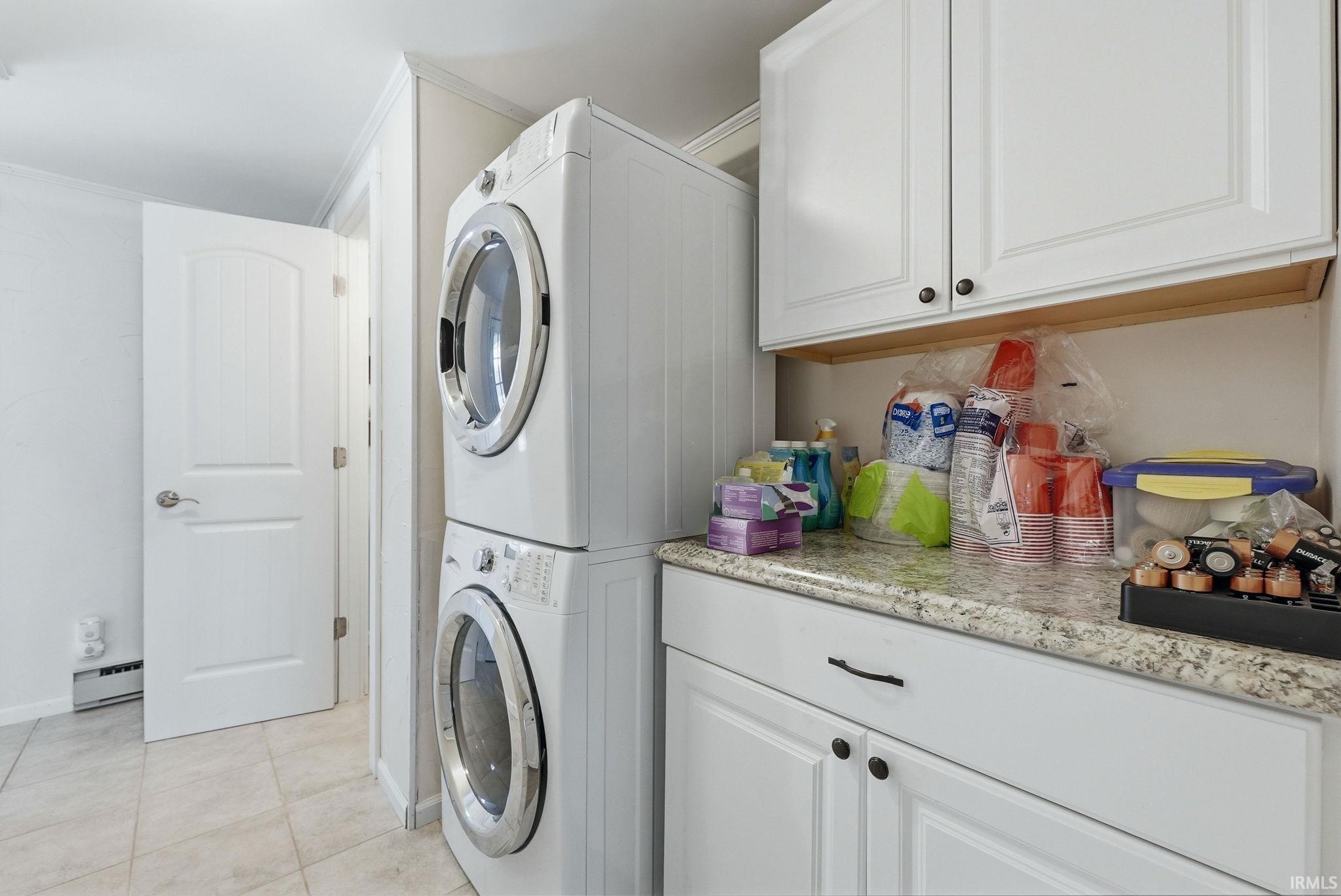 Laundry area featuring stacked washer / drying machine, baseboard heating, cabinet space, and light tile patterned floors