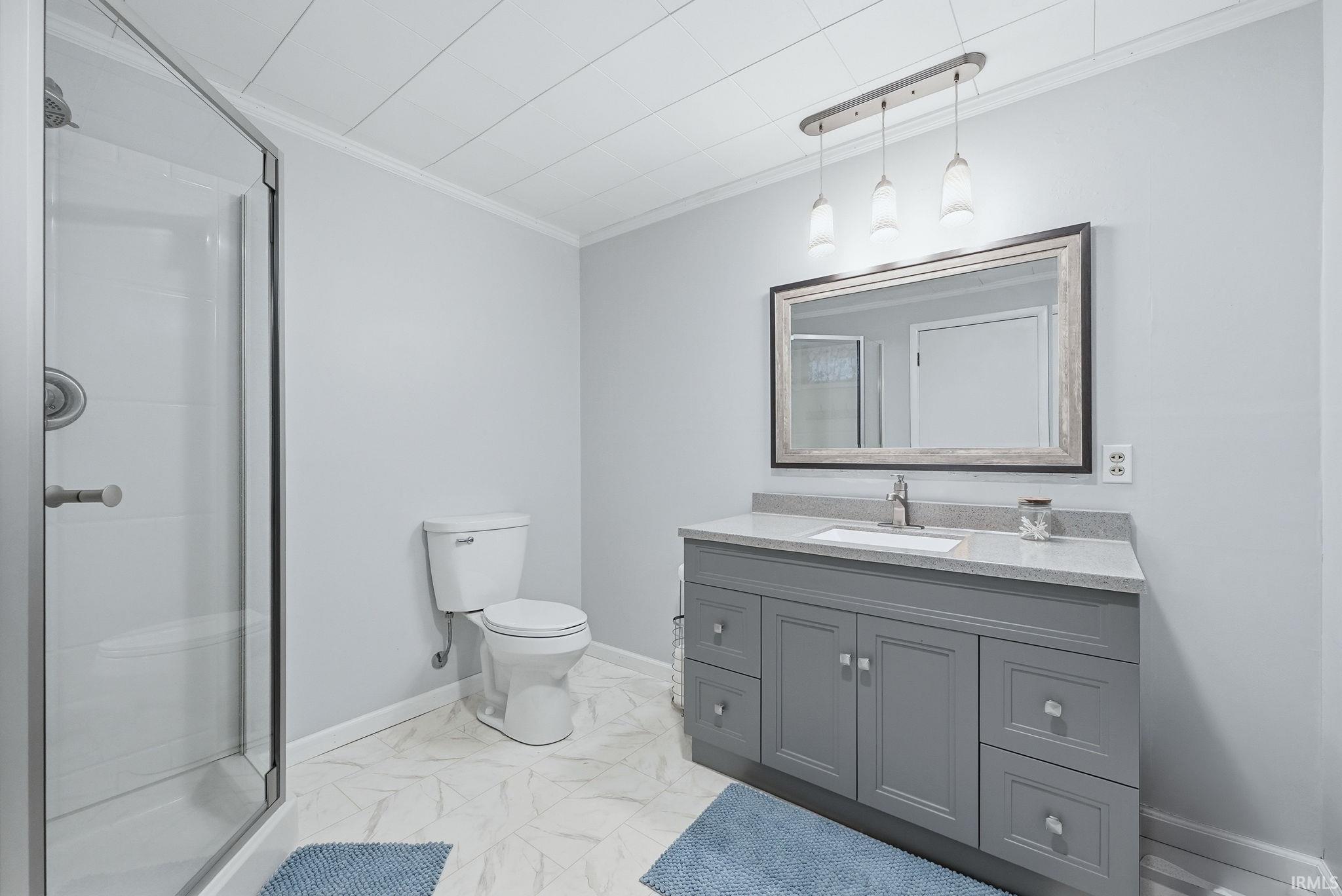 Full bathroom featuring light marble finish flooring, vanity, a shower stall, and ornamental molding
