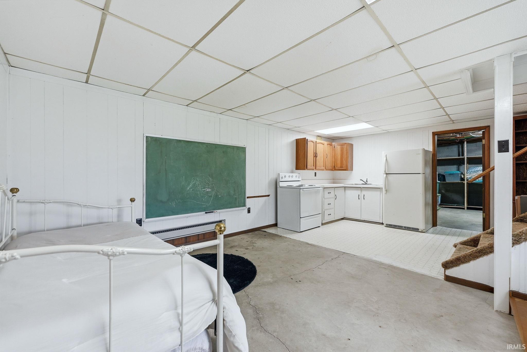 Interior space featuring freestanding refrigerator, a drop ceiling, wooden walls, and concrete floors