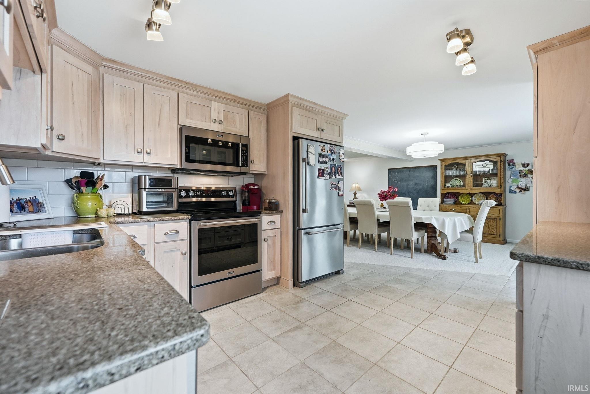 Kitchen featuring stainless steel appliances, dark stone countertops, tasteful backsplash, and light tile patterned flooring