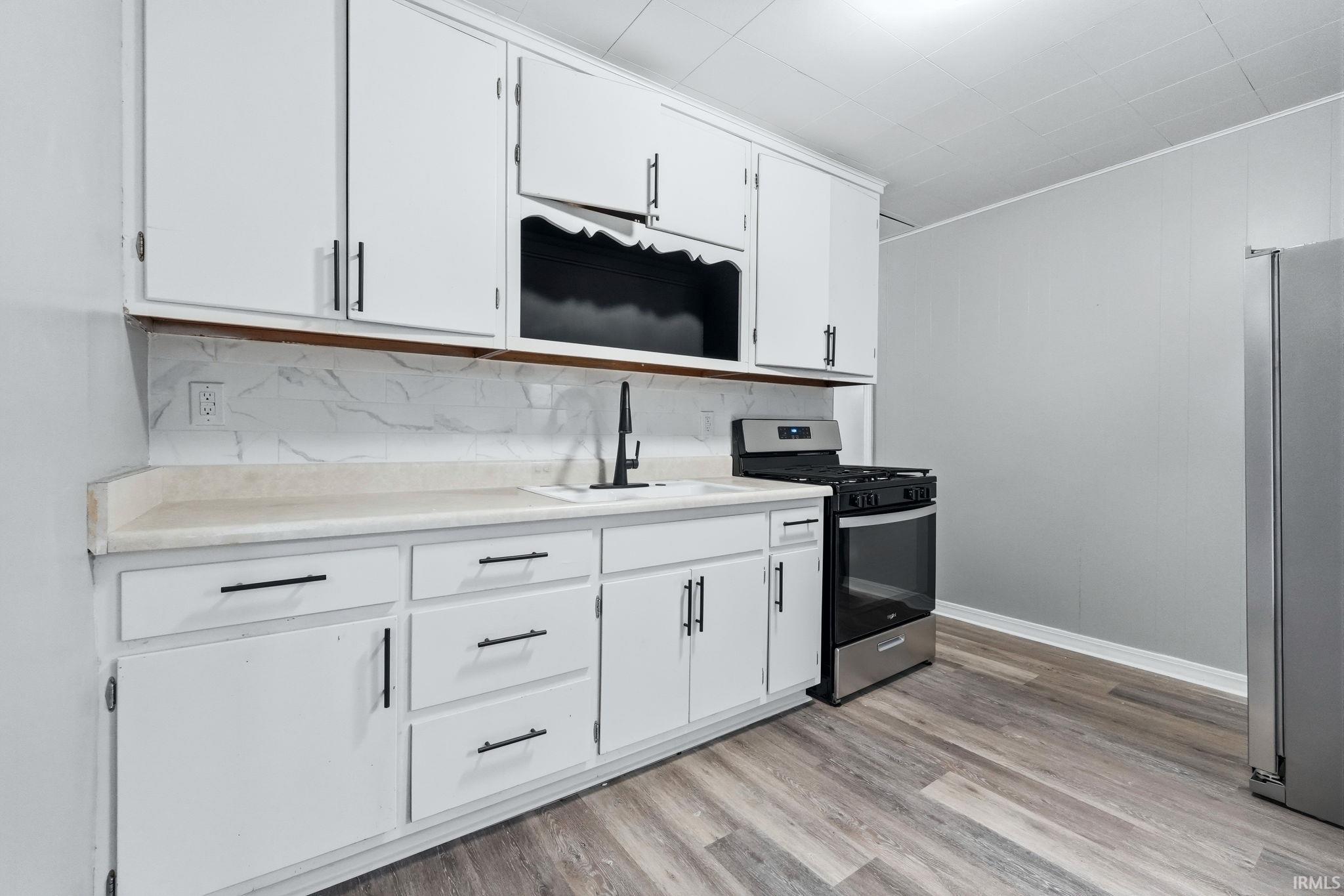 Kitchen with white cabinetry, stainless steel appliances, light countertops, and ornamental molding