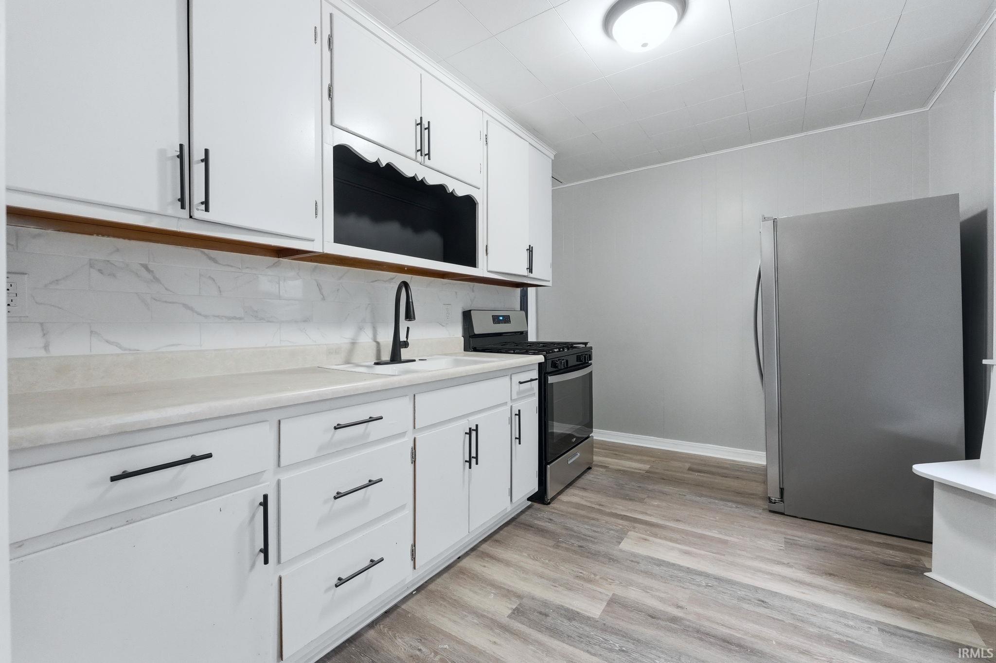 Kitchen featuring white cabinetry, stainless steel appliances, light countertops, light wood-style flooring, and tasteful backsplash
