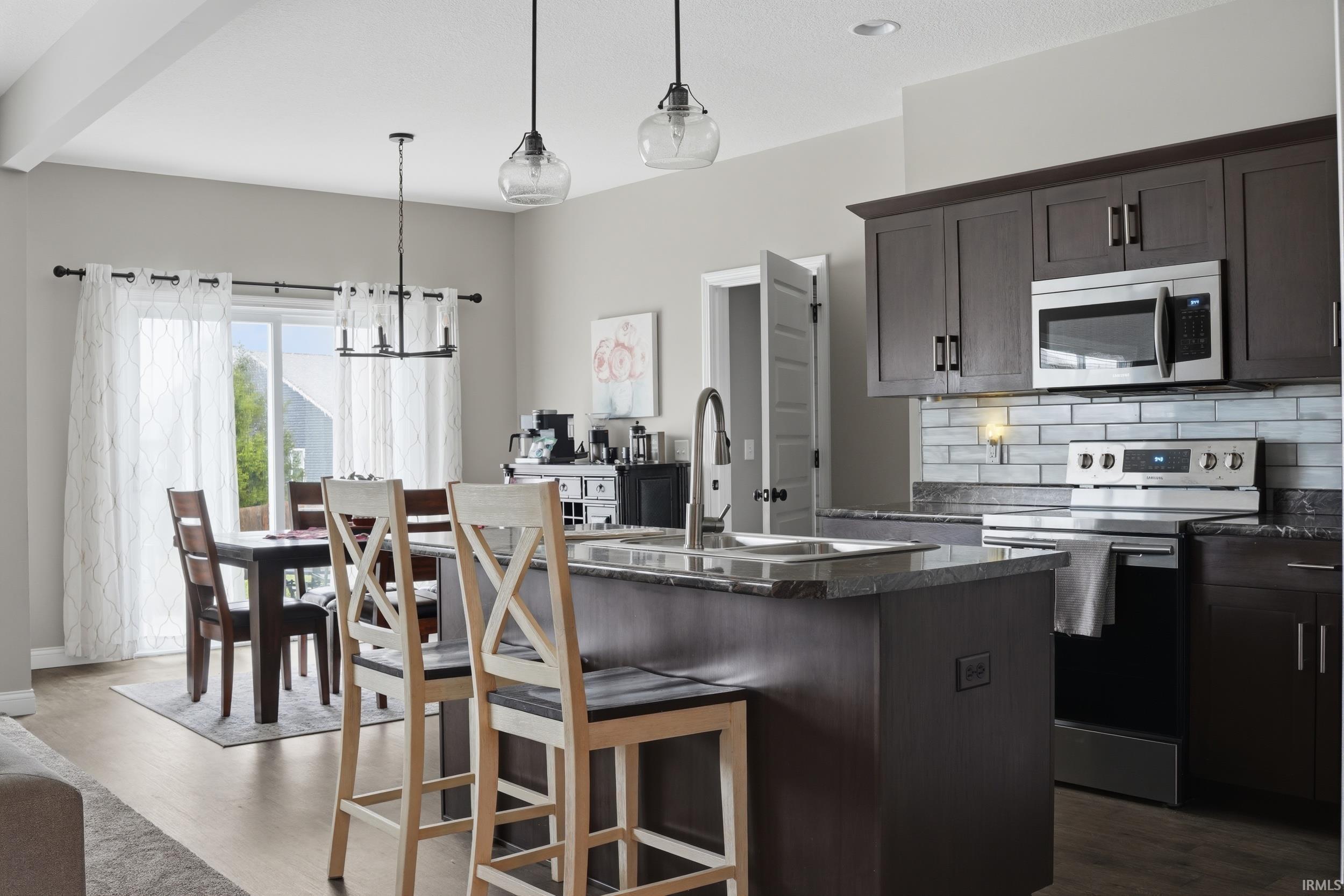 Kitchen featuring stainless steel appliances, dark wood finish cabinetry, tasteful backsplash, an island with sink, and a breakfast bar