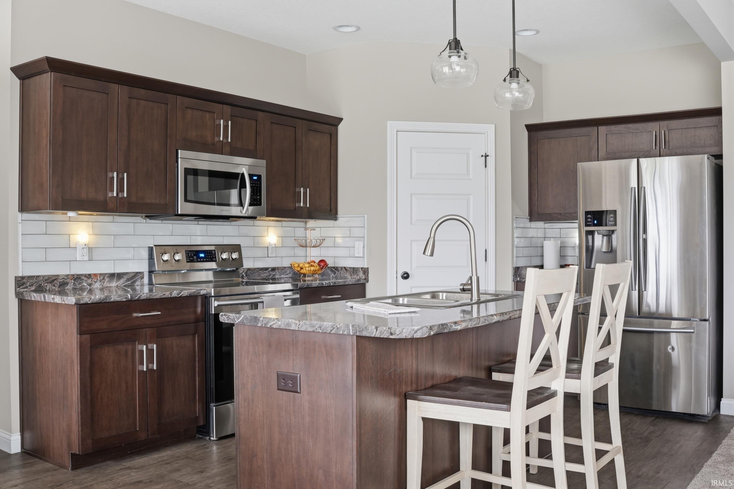 Kitchen featuring stainless steel appliances, dark stone counters, an island with sink, and dark wood finished floors