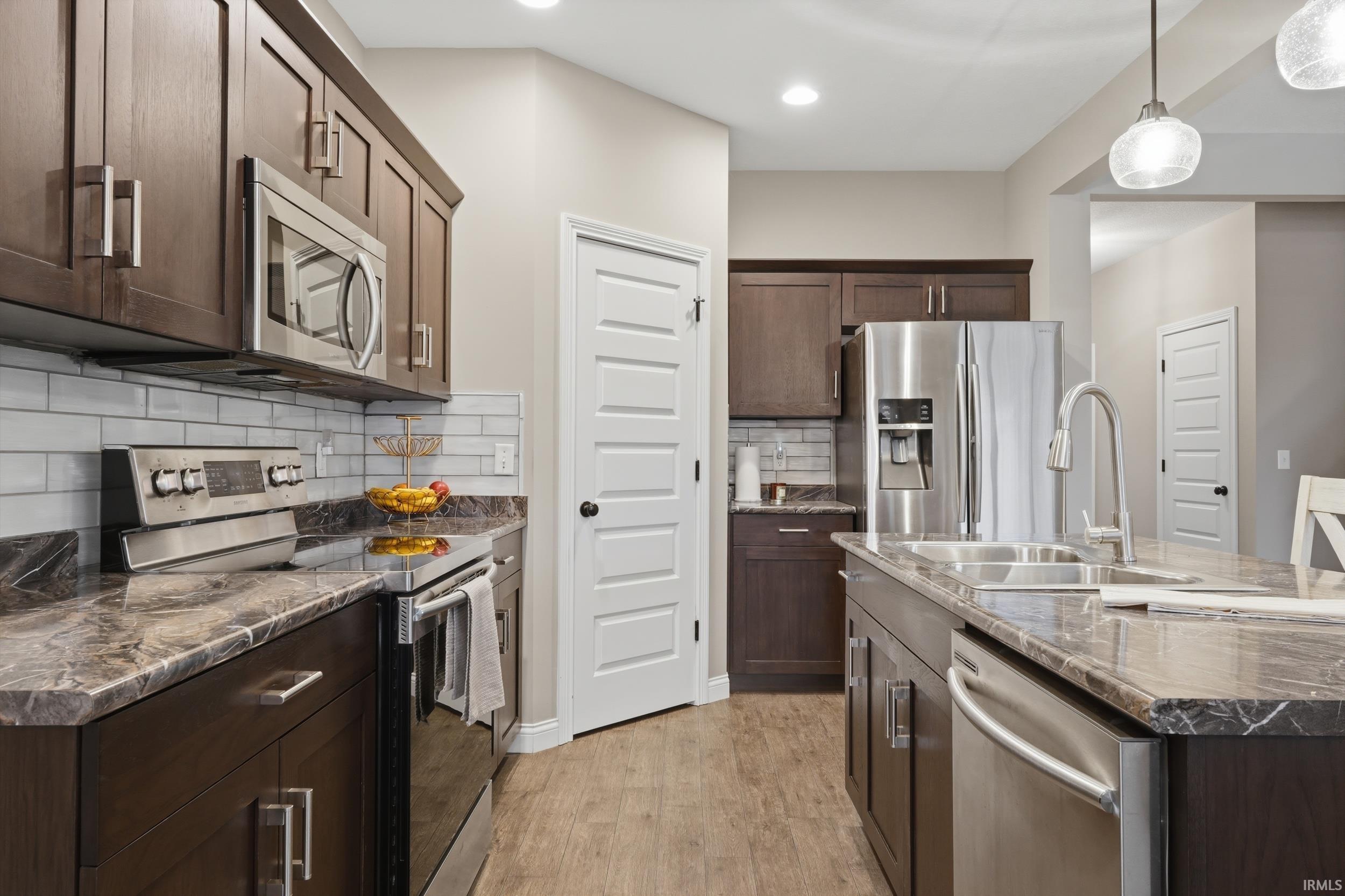 Kitchen featuring dark wood finish cabinets, stainless steel appliances, backsplash, dark stone countertops, and light wood-type flooring