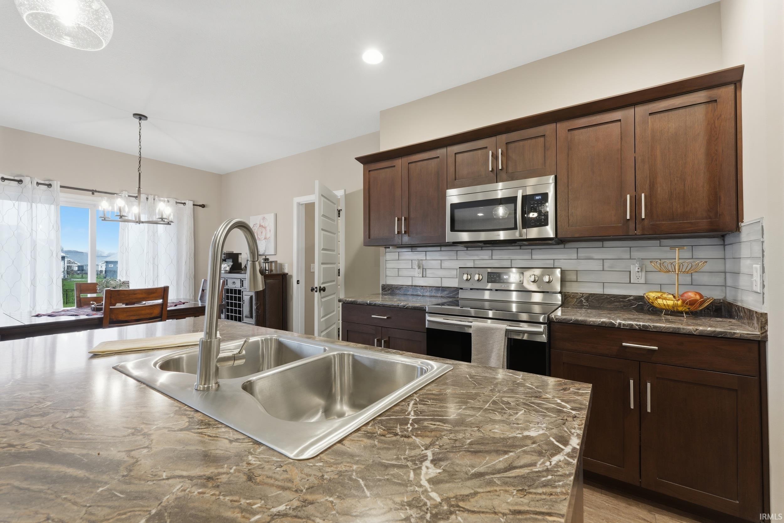 Kitchen with stainless steel appliances, dark wood finish cabinets, suspended lighting, and decorative backsplash