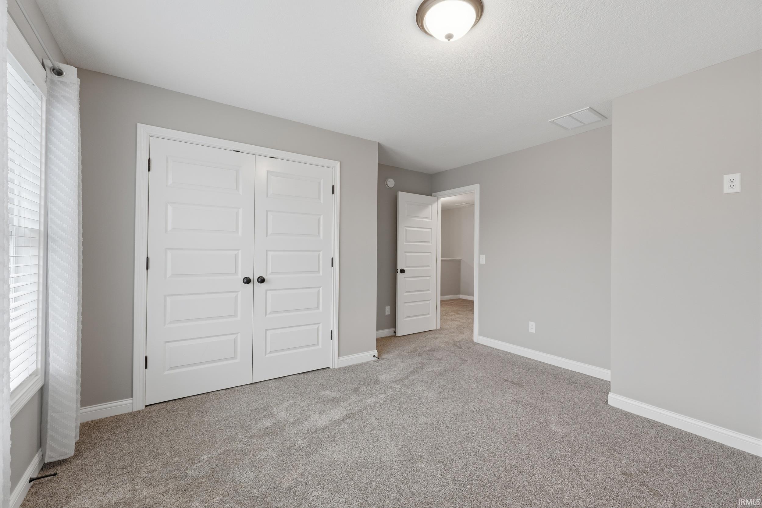 Unfurnished bedroom featuring a closet, light carpet, and multiple windows