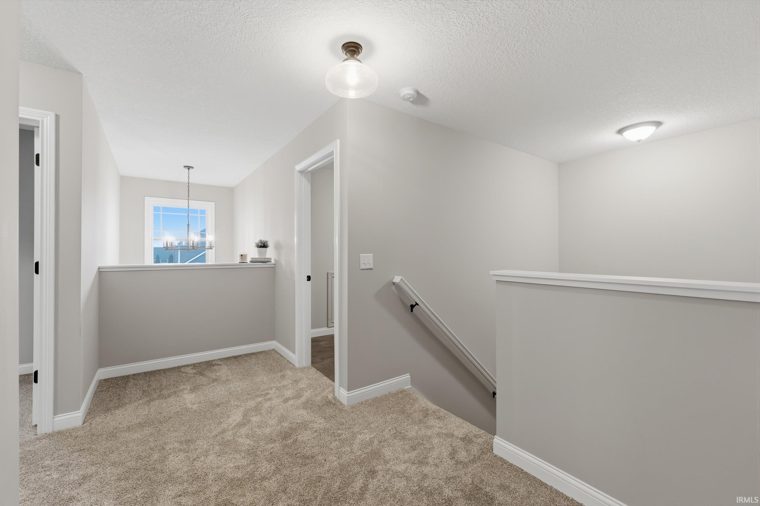 Corridor featuring an upstairs landing, light carpet, and a textured ceiling
