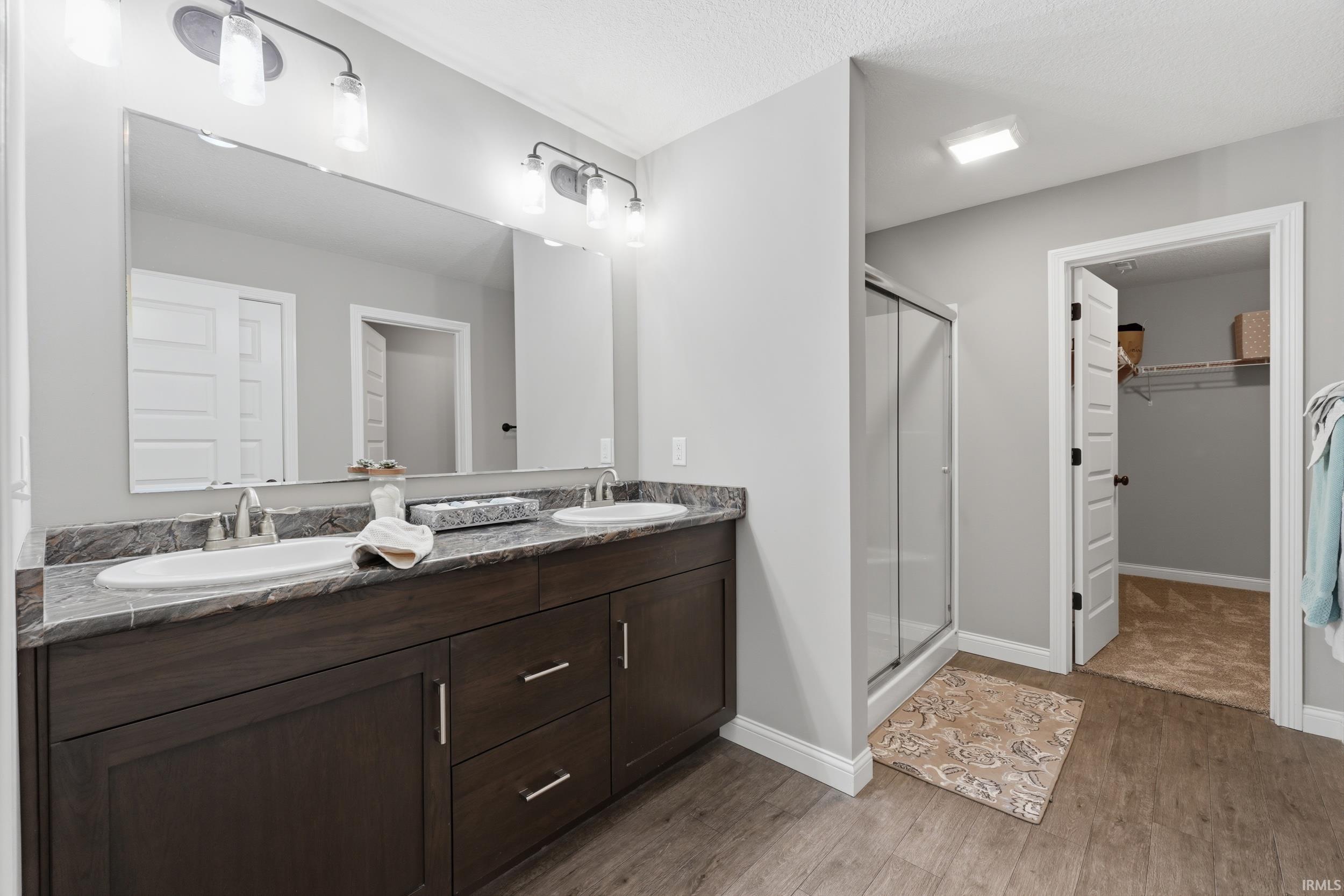 Bathroom featuring a spacious closet, double vanity, a stall shower, and light wood-style flooring