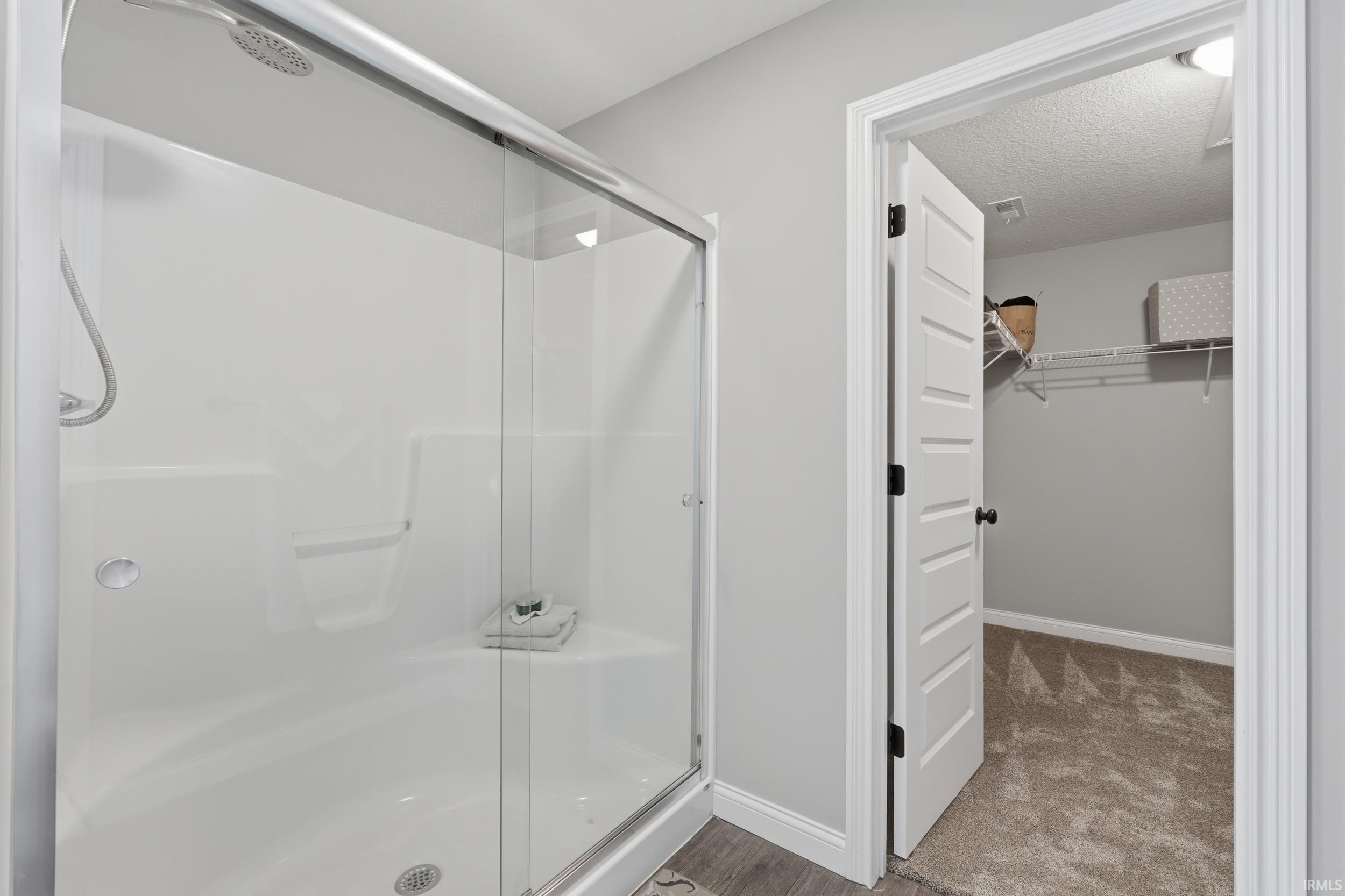 Bathroom featuring a walk in closet, a stall shower, and a textured ceiling