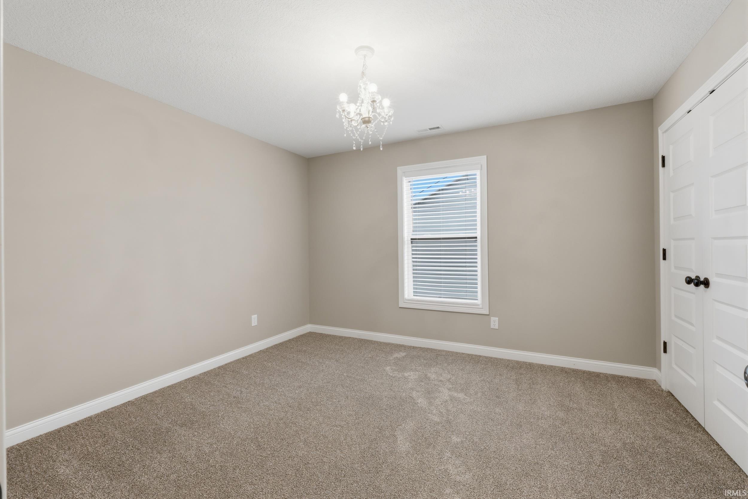 Unfurnished bedroom with a closet, light carpet, and hanging lights
