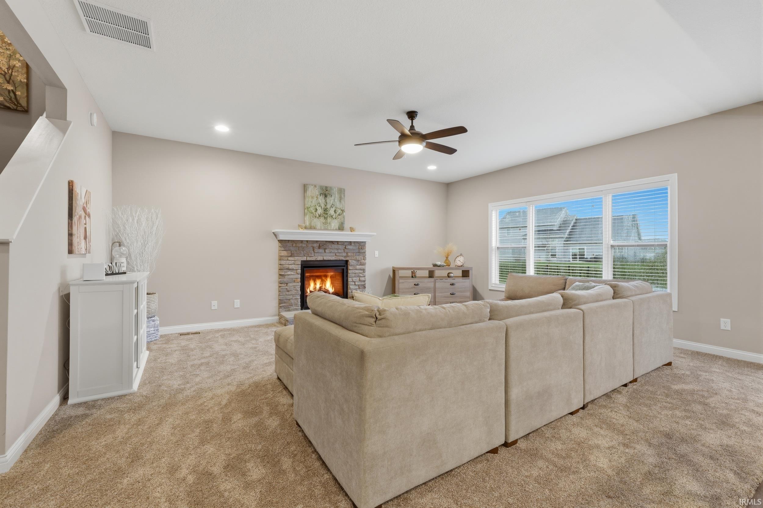 Living room with ceiling fan, light colored carpet, a stone fireplace, and recessed lighting