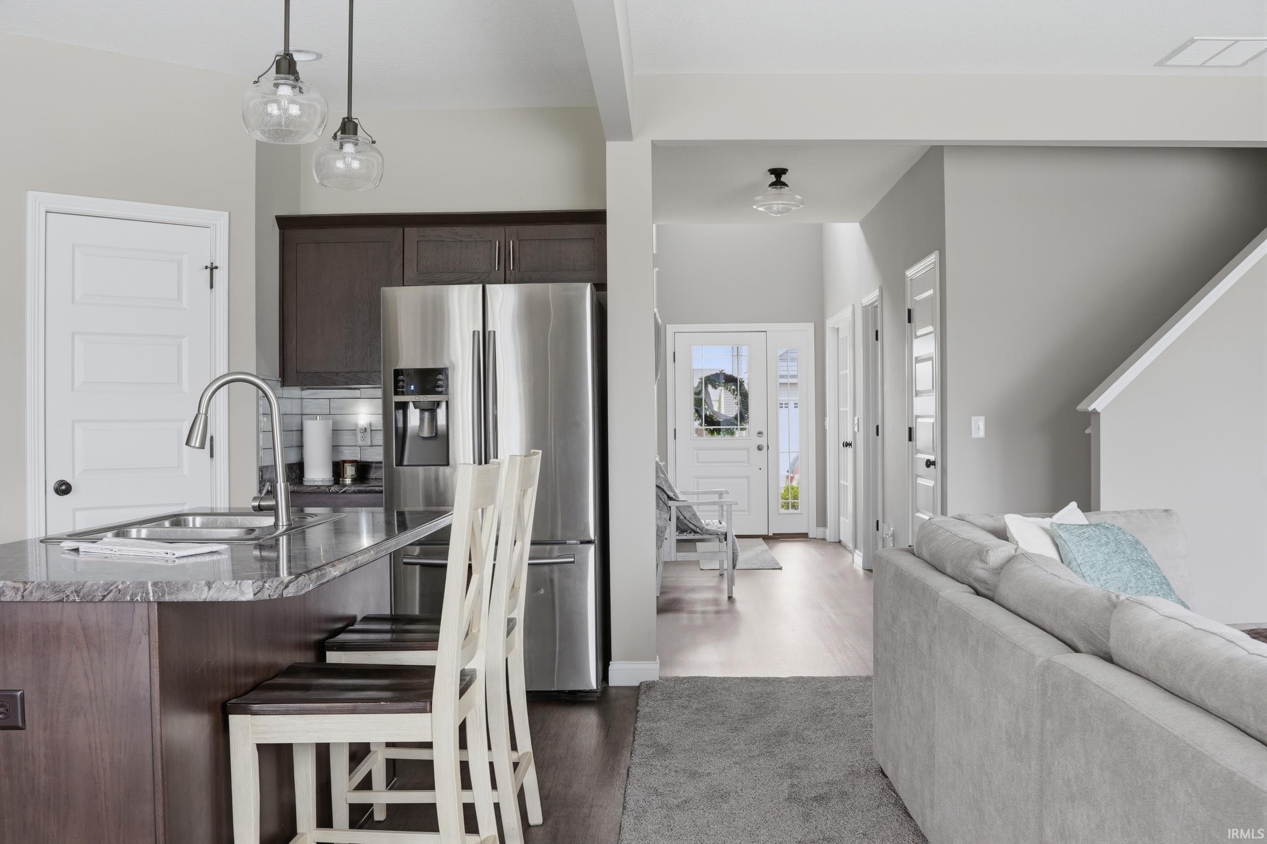 Kitchen featuring dark wood finish cabinets, stainless steel fridge, dark stone counters, dark wood-style floors, and open floor plan