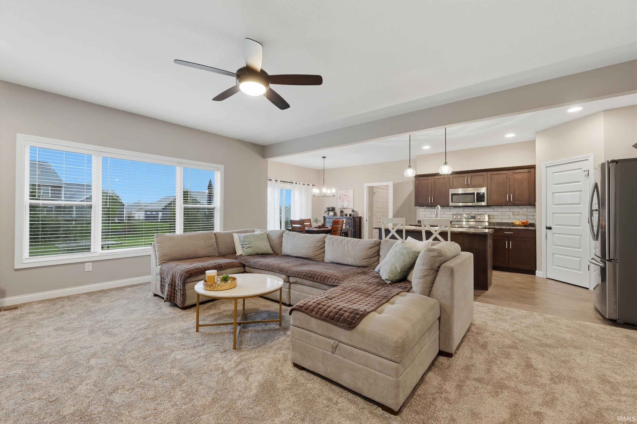 Living room with ceiling fan, light colored carpet, and a chandelier