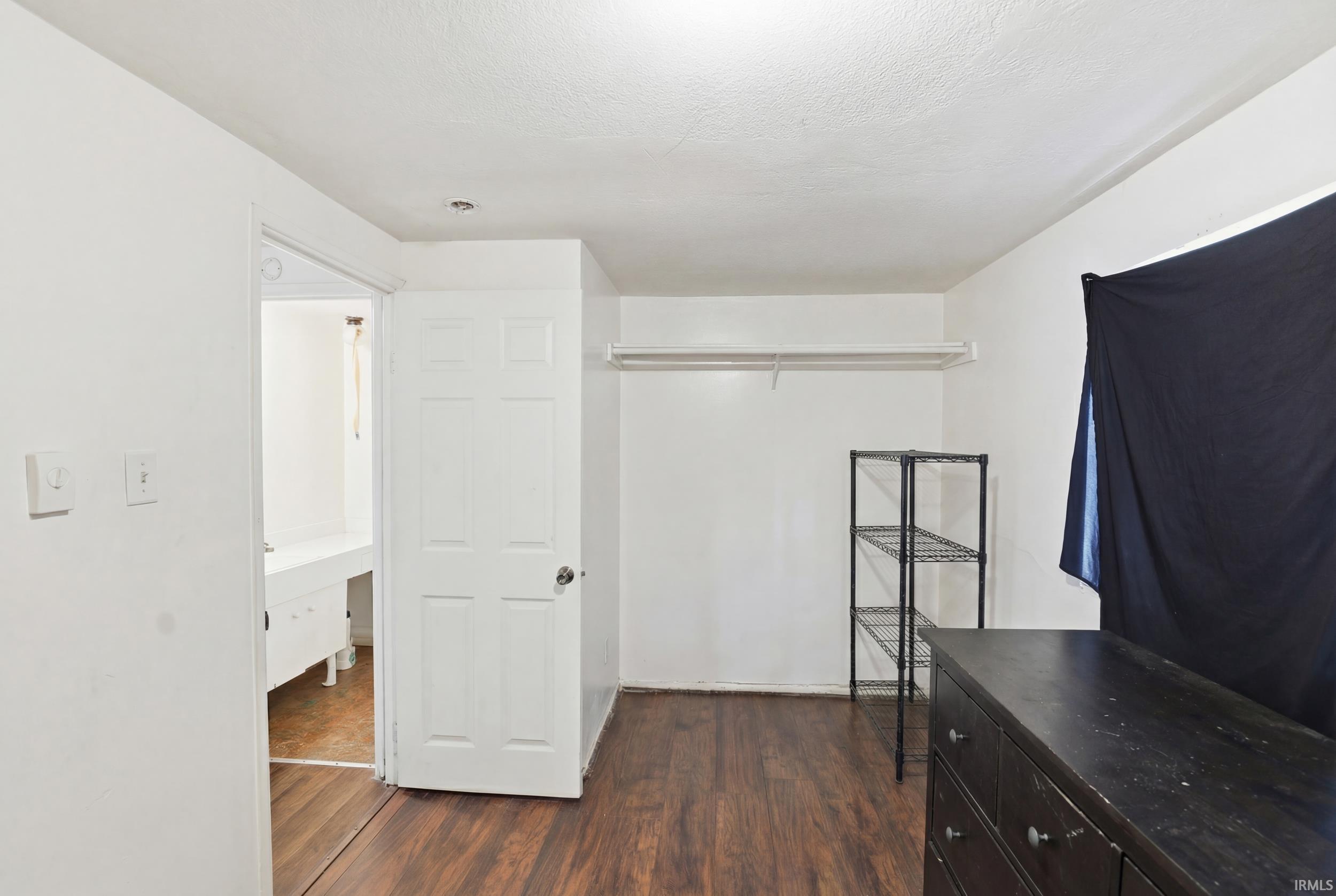 Unfurnished bedroom featuring dark wood-style flooring, a desk, and a closet