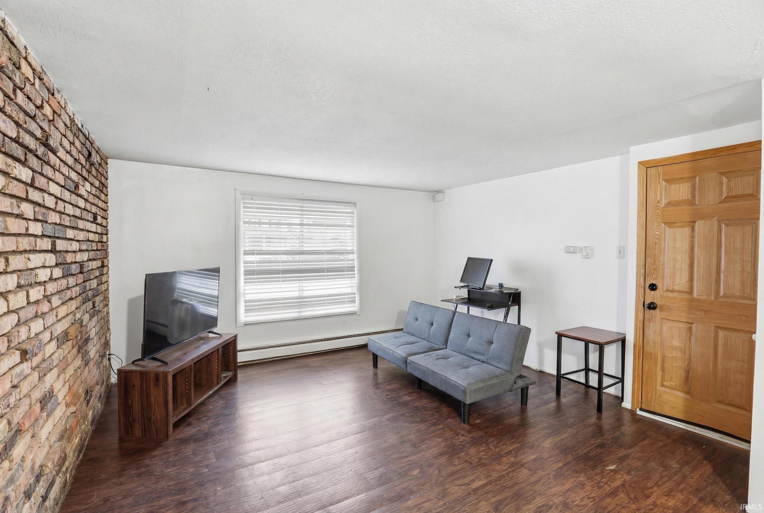 Sitting room with wood finished floors, brick wall, and a baseboard radiator