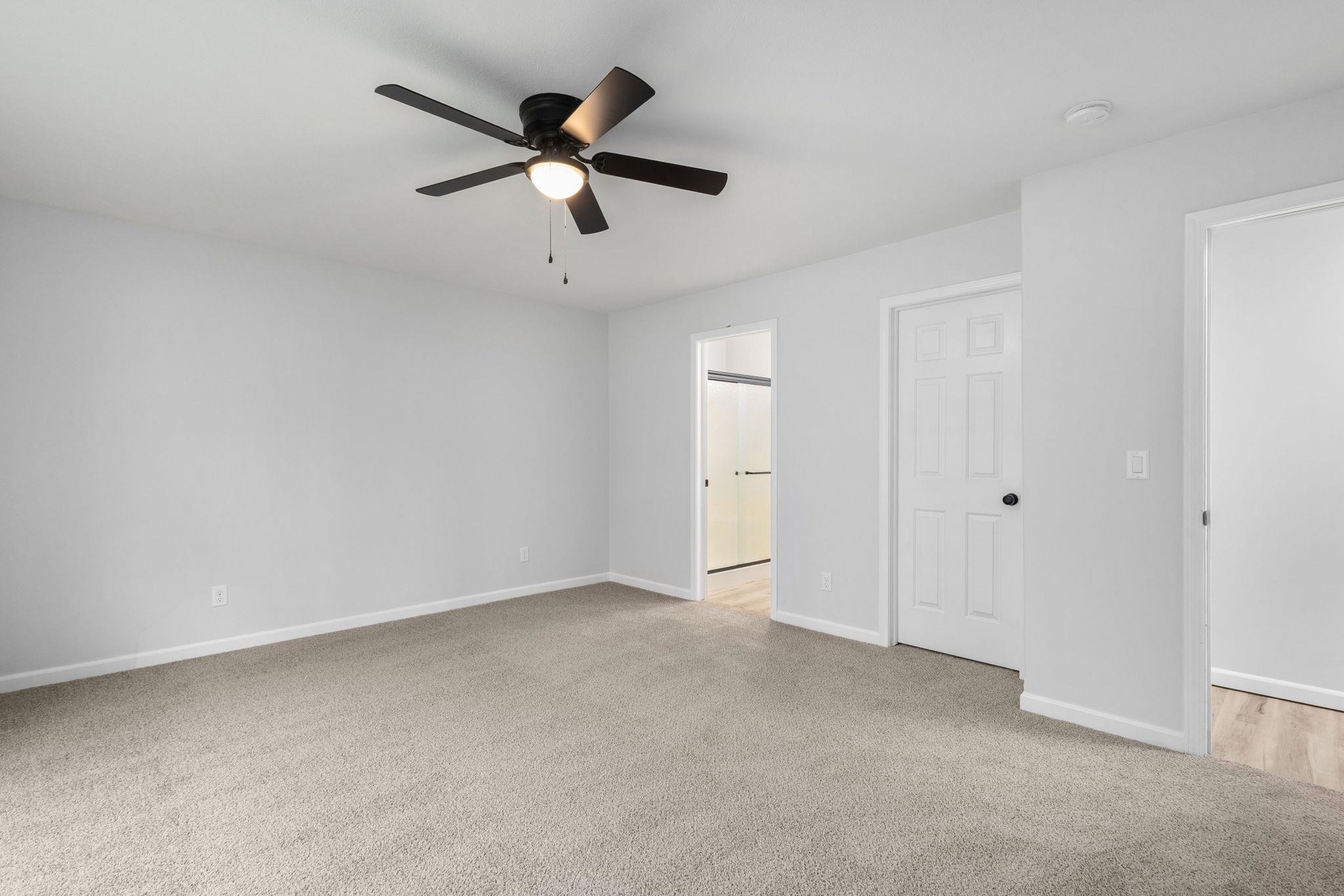 Unfurnished bedroom featuring light colored carpet, ceiling fan, and ensuite bathroom