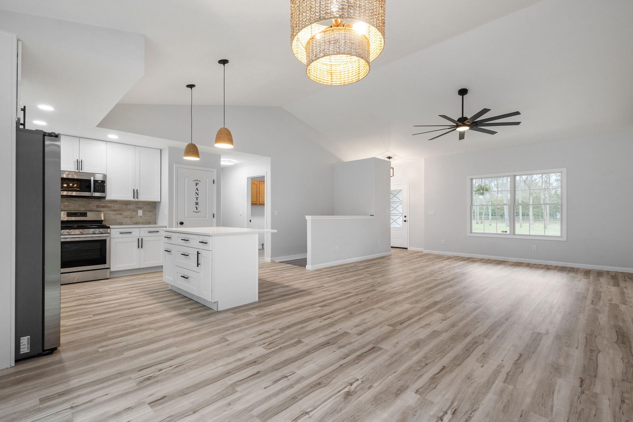 Kitchen featuring white cabinetry, stainless steel appliances, open floor plan, light countertops, and a kitchen island
