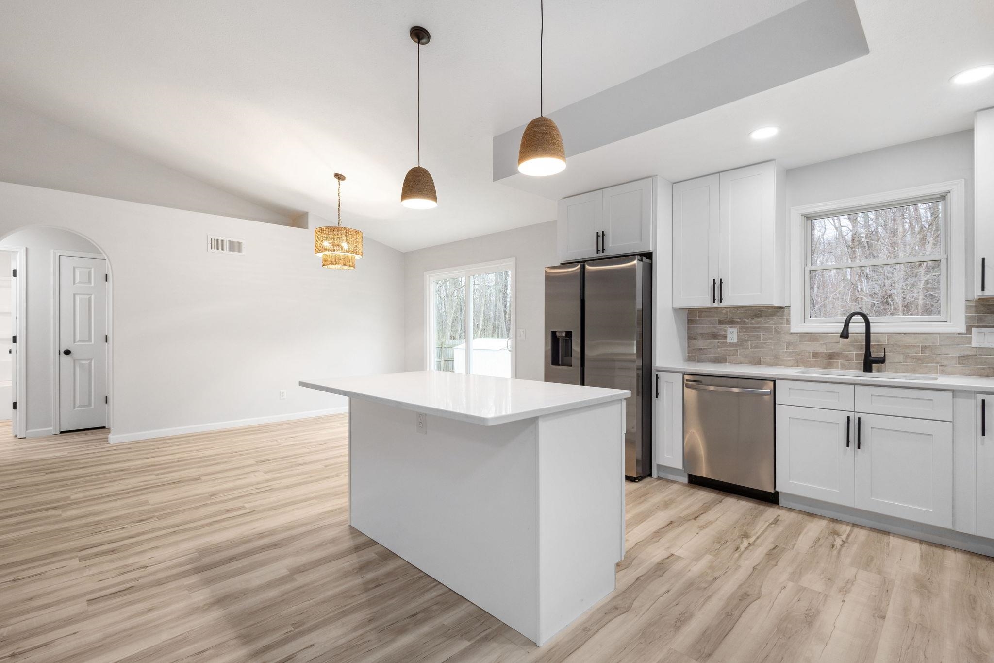 Kitchen with arched walkways, white cabinets, stainless steel appliances, decorative light fixtures, and light wood-type flooring