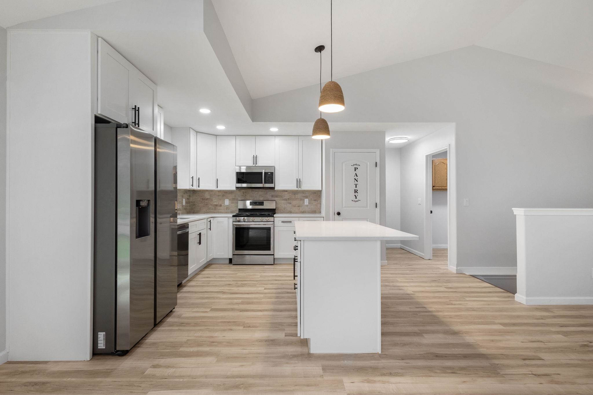 Kitchen with white cabinetry, stainless steel appliances, decorative light fixtures, tasteful backsplash, and light wood-style flooring