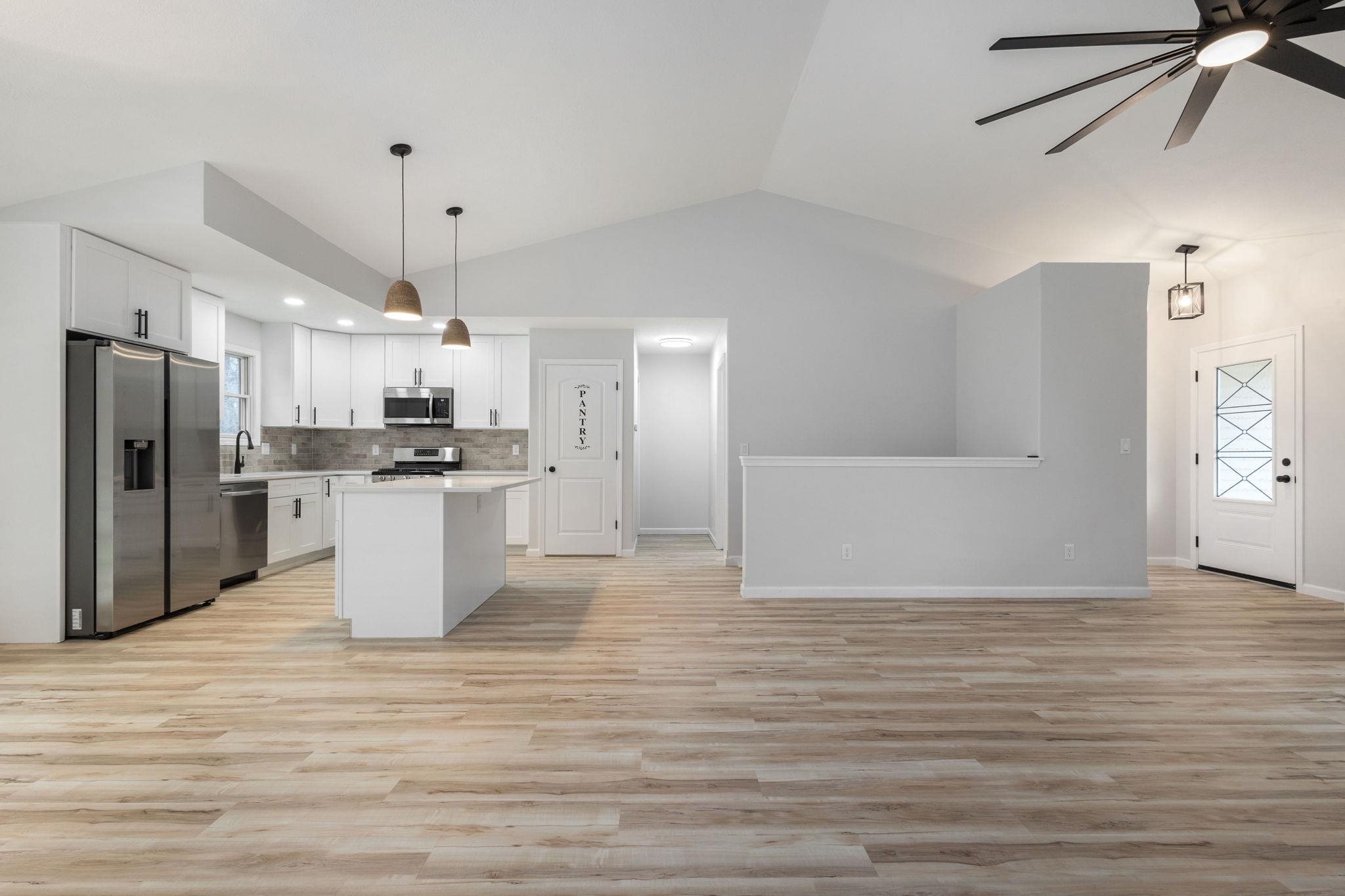 Kitchen with white cabinets, stainless steel appliances, pendant lighting, open floor plan, and vaulted ceiling