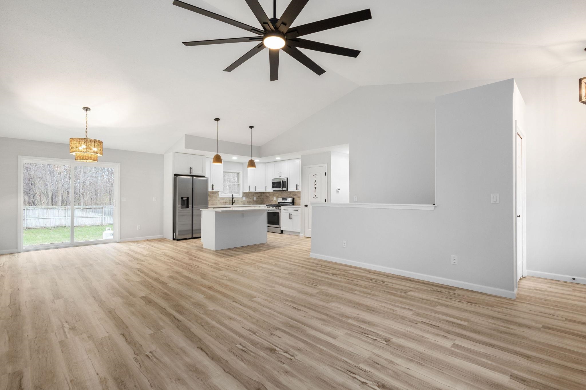 Unfurnished living room featuring suspended lighting, vaulted ceiling, light wood-type flooring, and a ceiling fan