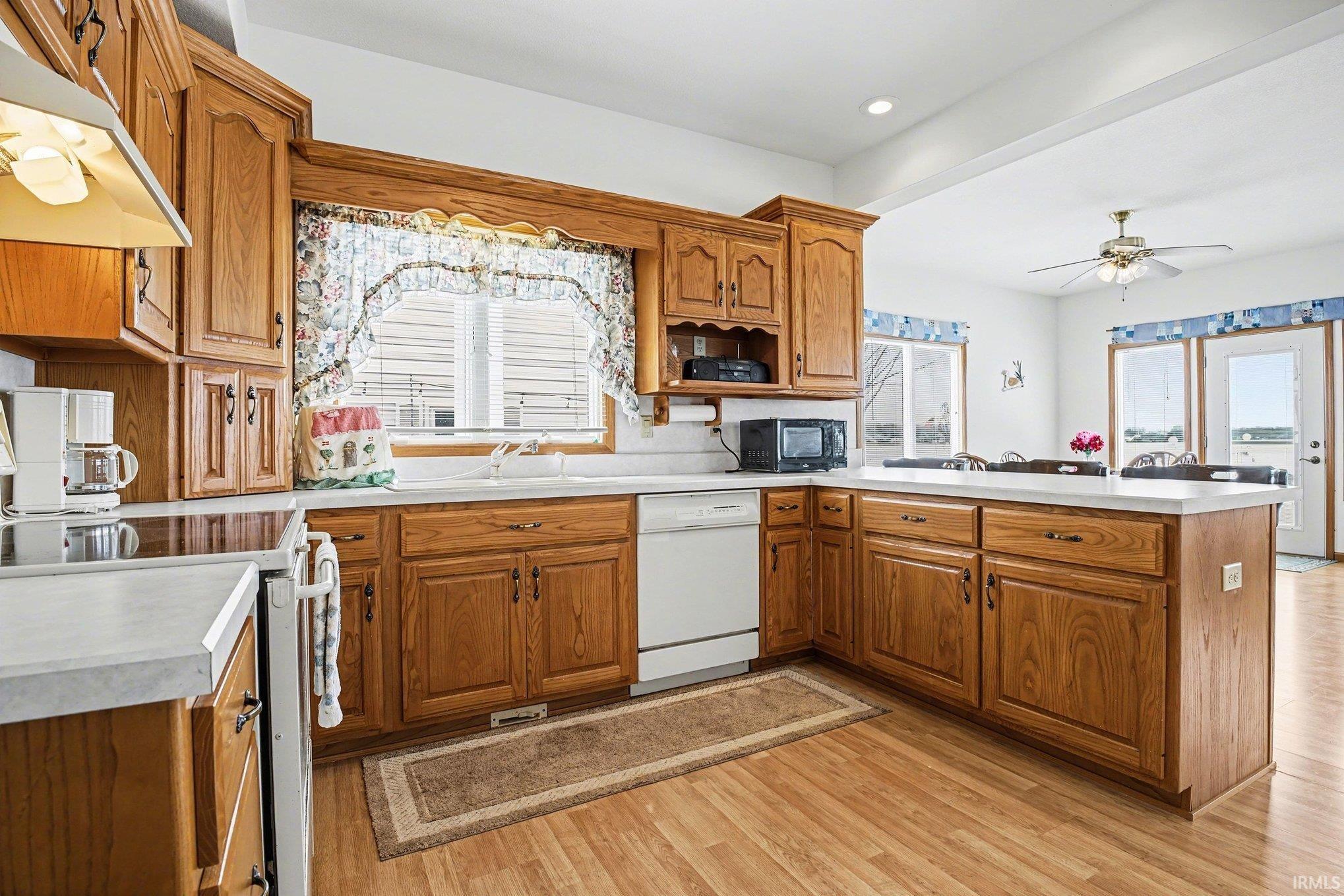 Kitchen with light countertops, a peninsula, wood finish cabinetry, light wood finished floors, and white dishwasher