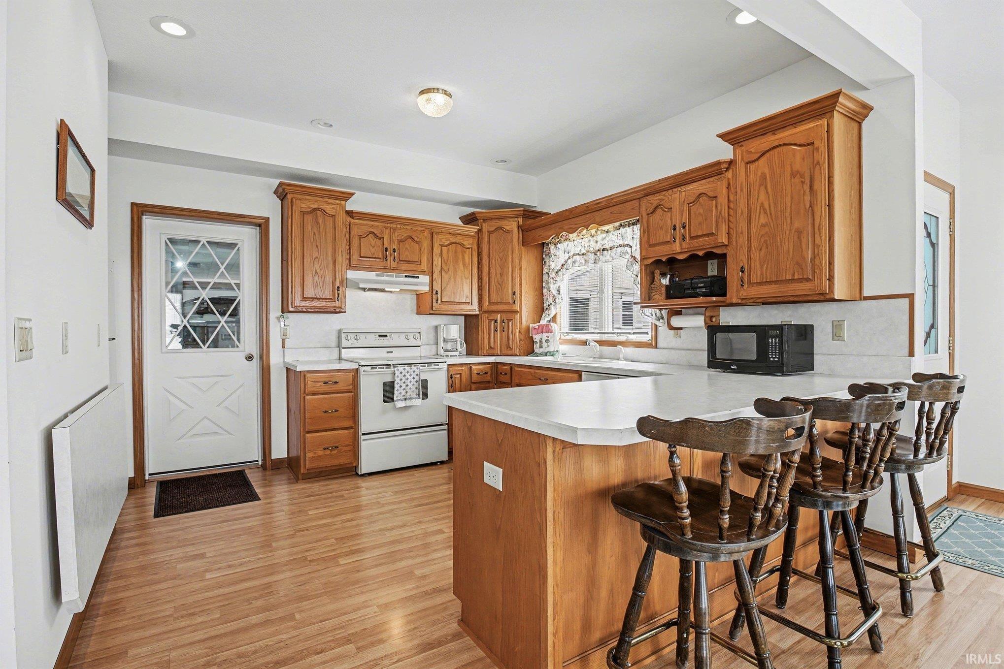 Kitchen with a kitchen bar, a peninsula, white electric range, wood finish cabinetry, and recessed lighting