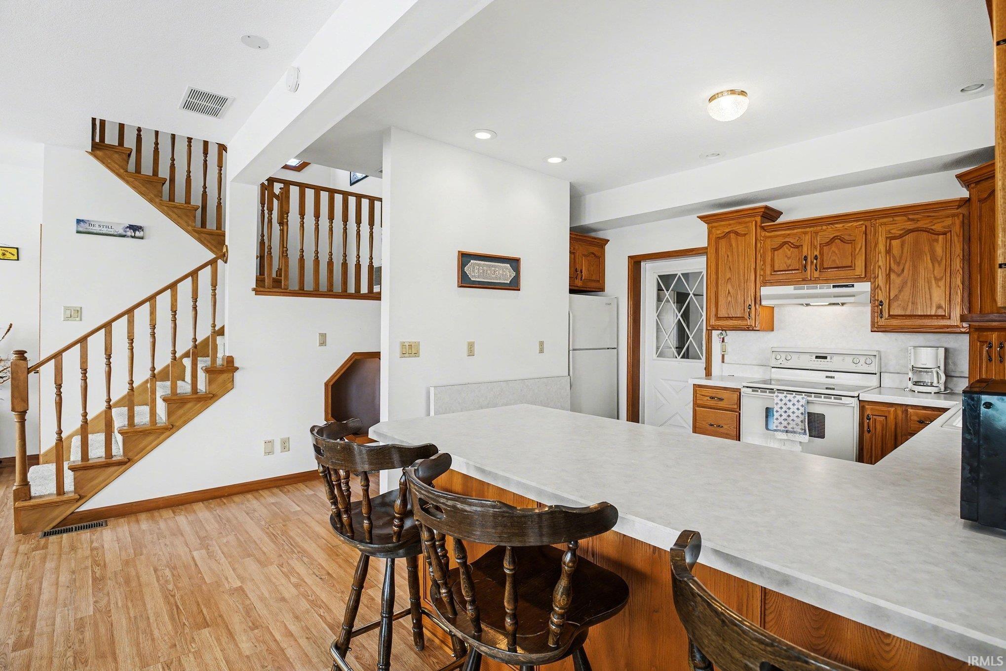 Kitchen featuring light countertops, wood finish cabinets, white appliances, a peninsula, and a breakfast bar