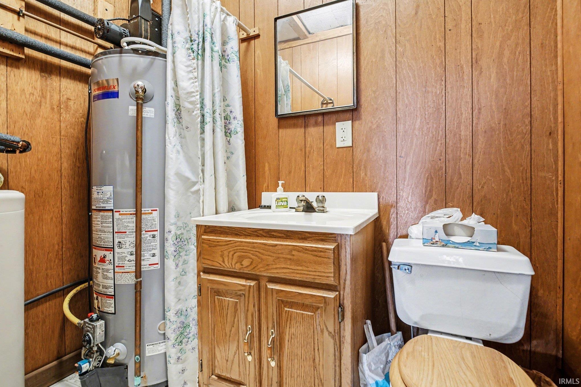 Bathroom featuring wood walls, vanity, a stall shower, and gas water heater