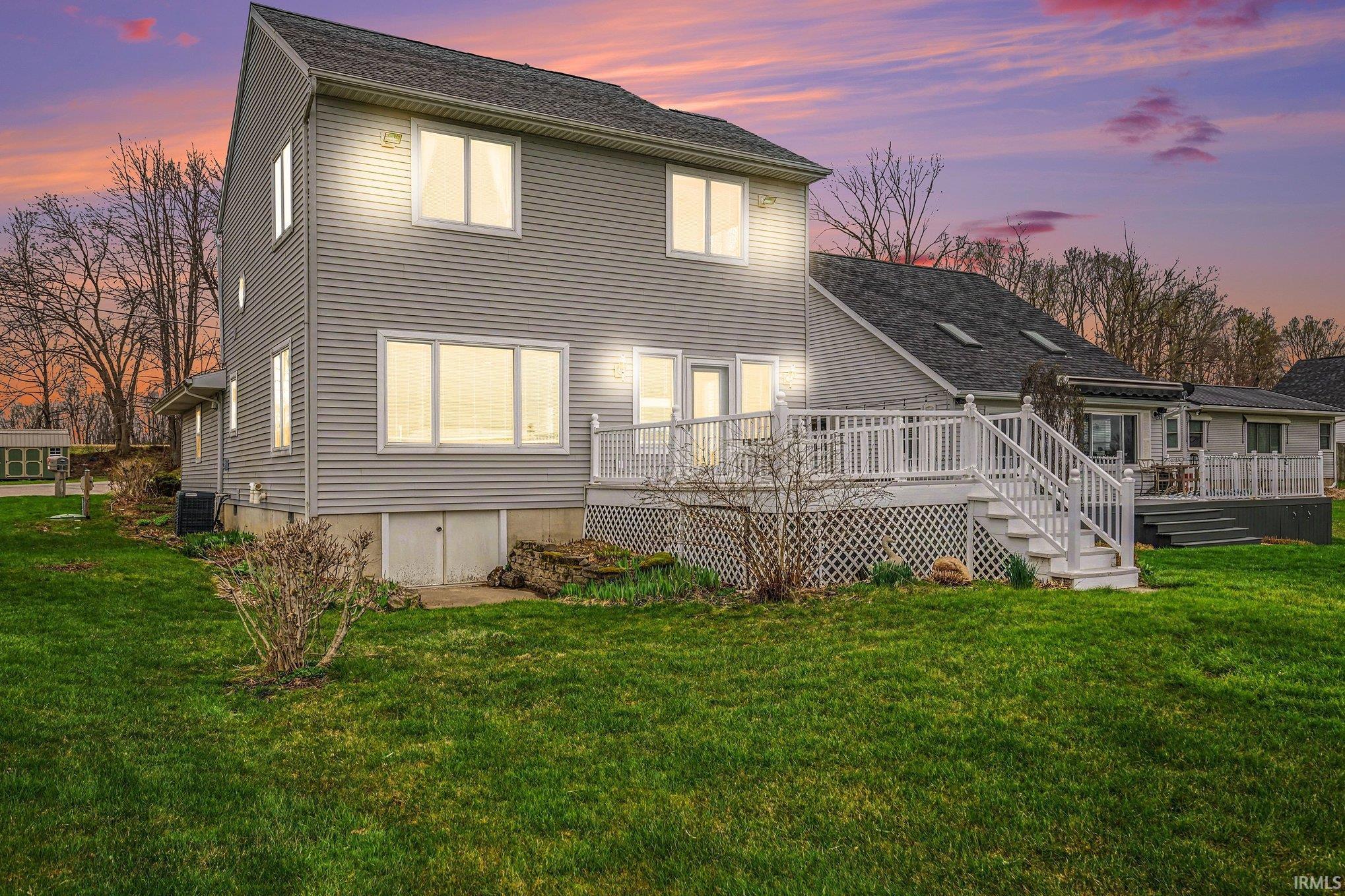 Back of property at dusk with a lawn, a wooden deck, and a shingled roof