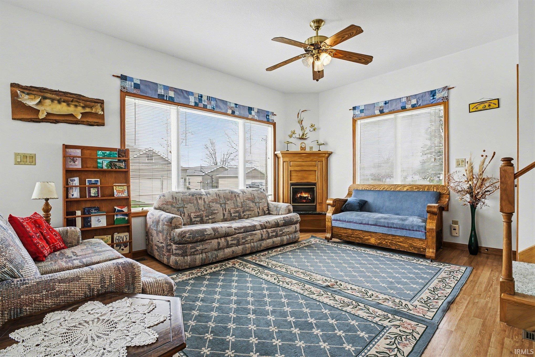 Living room featuring hardwood / wood-style flooring, ceiling fan, plenty of natural light, and a warm lit fireplace