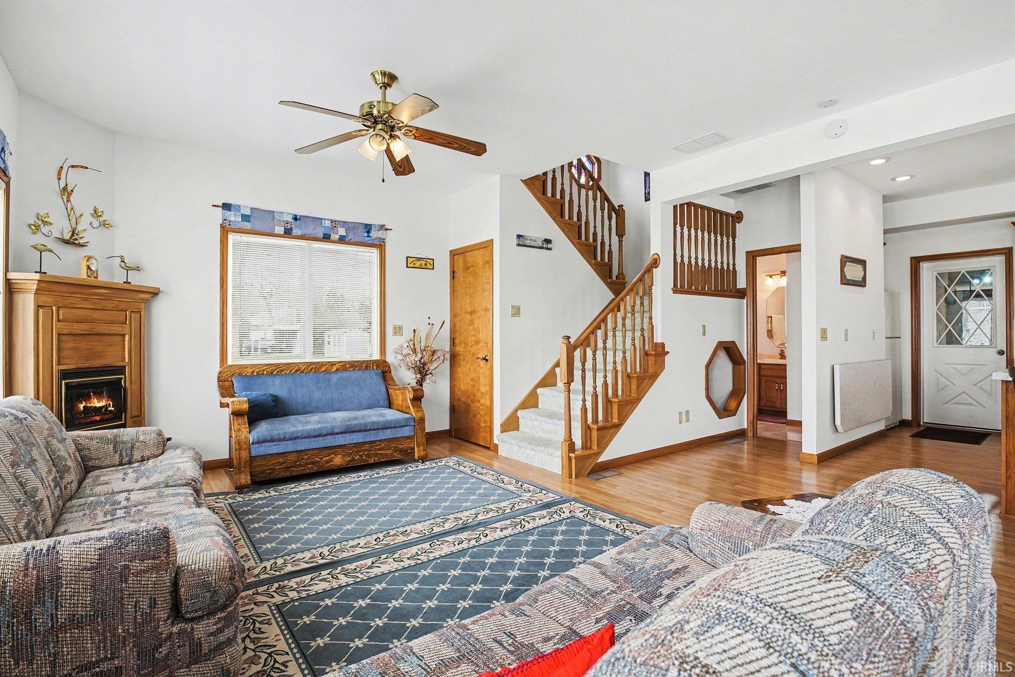 Living room featuring wood finished floors, ceiling fan, a lit fireplace, and recessed lighting