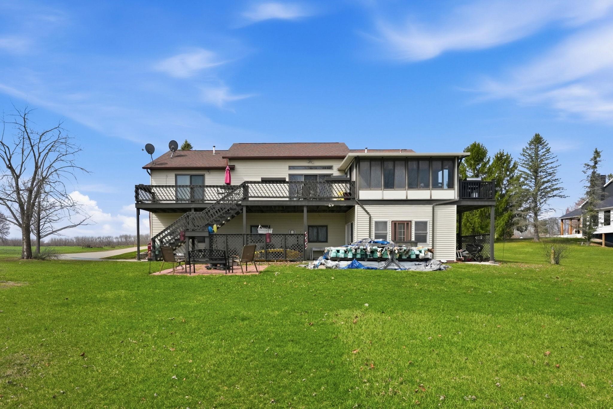 Back of property featuring a wooden deck, a patio, a yard, and a sunroom