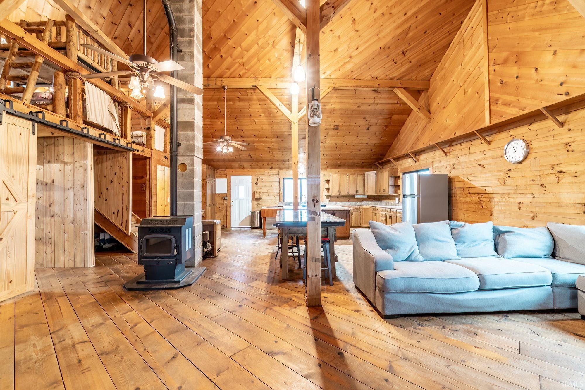 Living room featuring wood walls, light wood-style floors, a high wood beamed ceiling, a wood stove, and a barn door