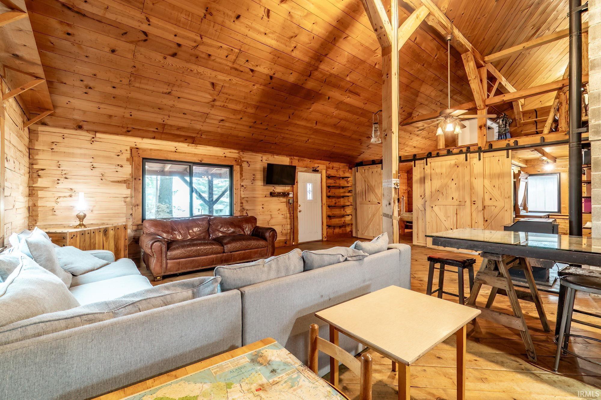 Living area with hardwood / wood-style flooring, wooden walls, a vaulted wood ceiling, and ceiling fan