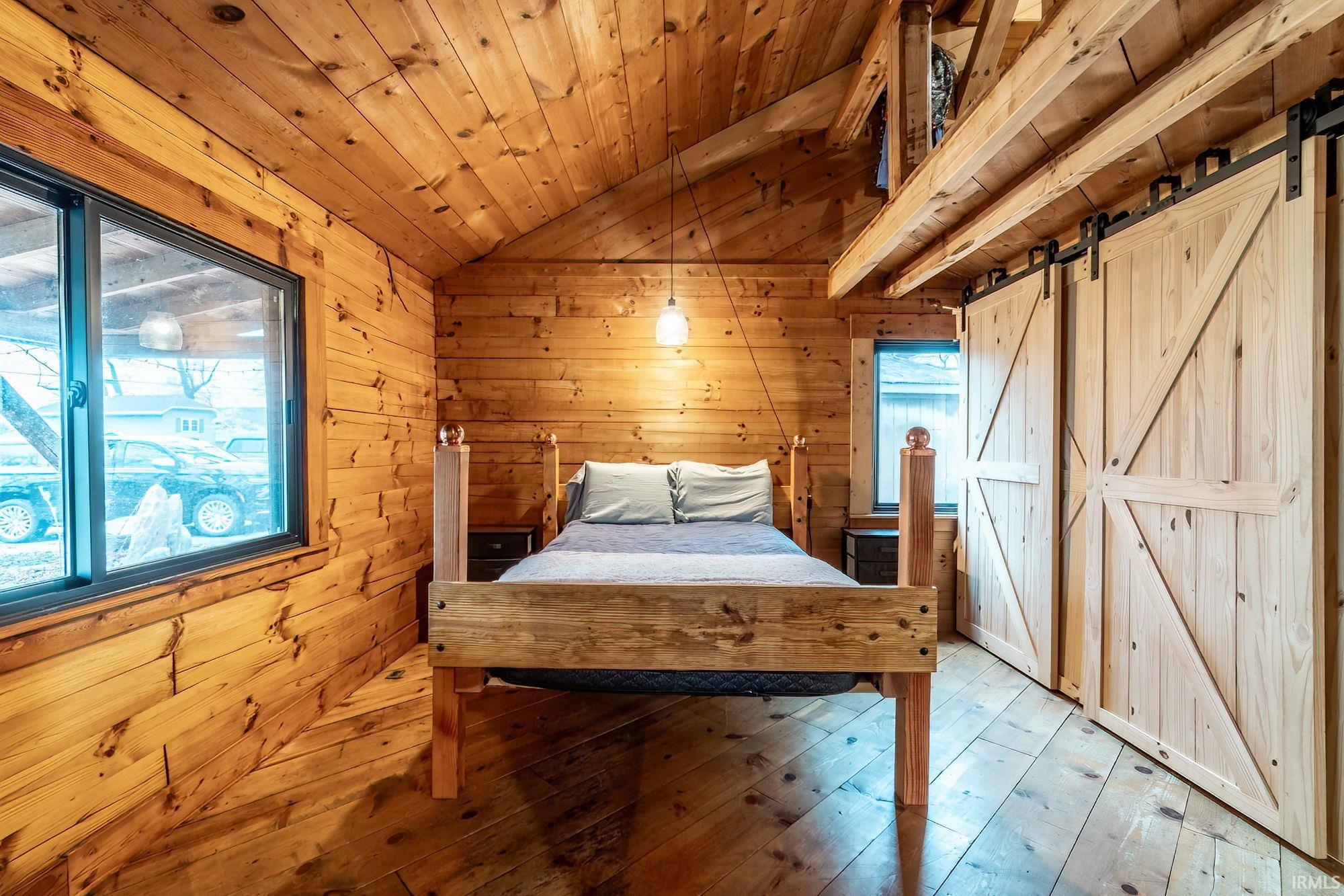 Bedroom with a barn door, wood-type flooring, wooden walls, and a vaulted wood ceiling