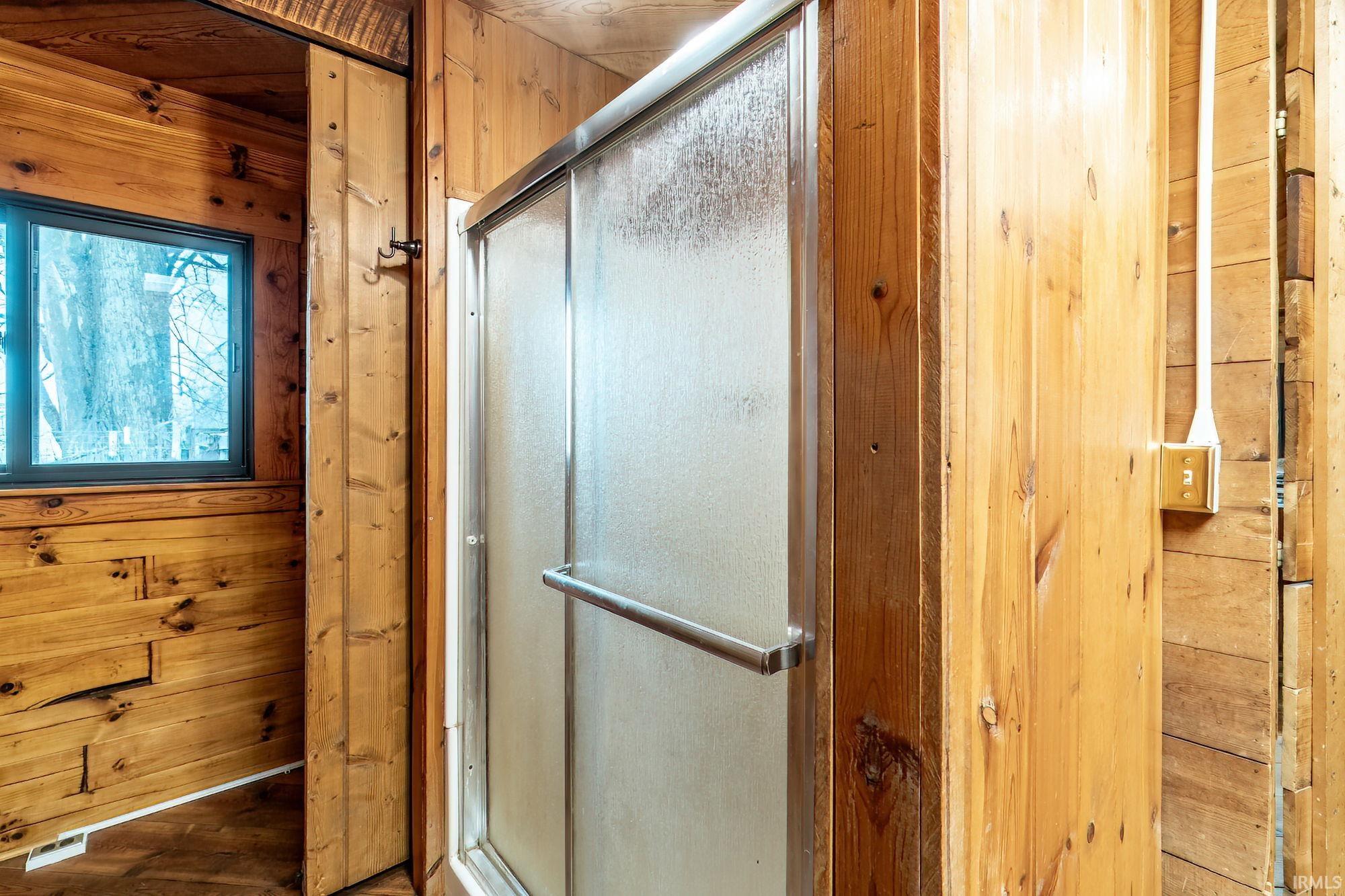 Full bathroom with a stall shower, wooden walls, and wood finished floors