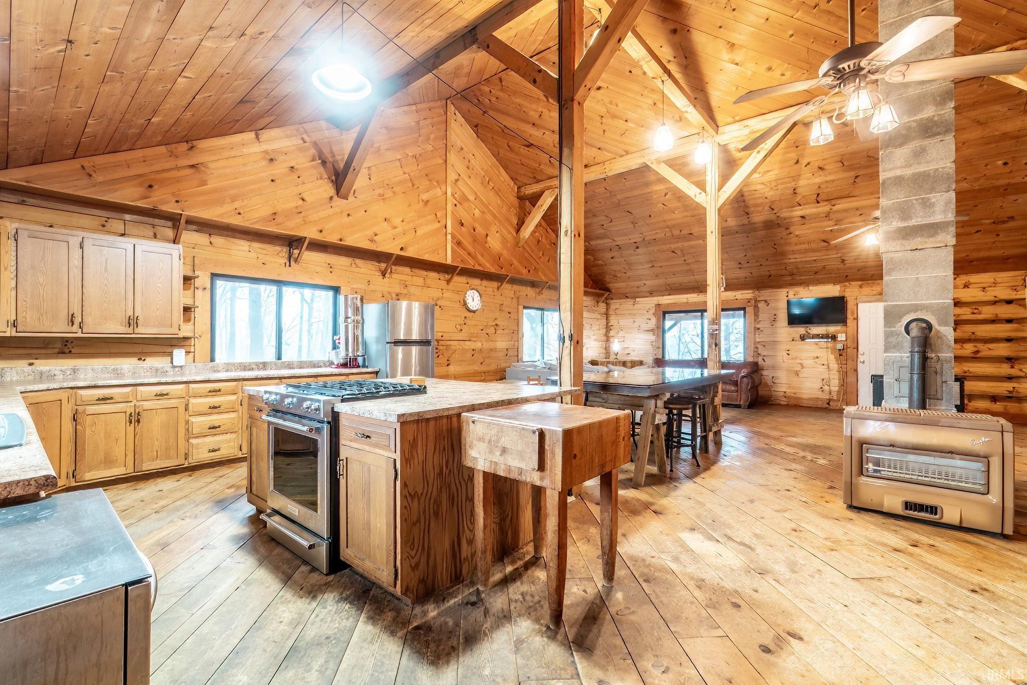 Kitchen with wooden walls, a vaulted wooden ceiling, stainless steel appliances, light countertops, and light wood-style floors