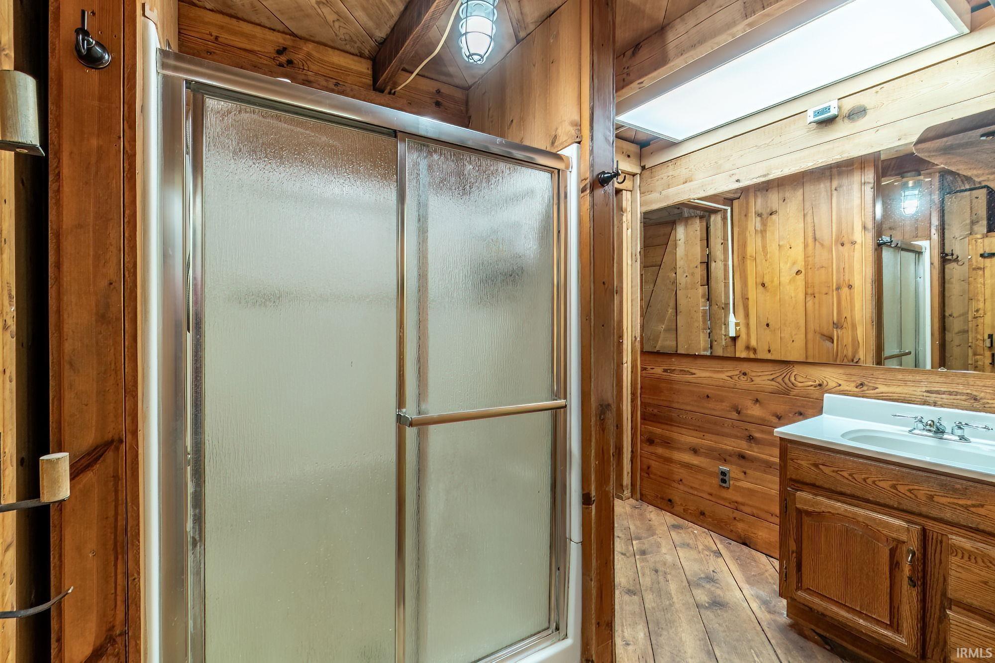 Bathroom with wood walls, vanity, a shower stall, and light wood finished floors