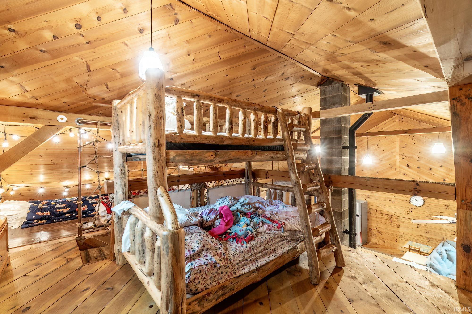 Bedroom with a vaulted wooden ceiling, wood walls, and light wood-style floors