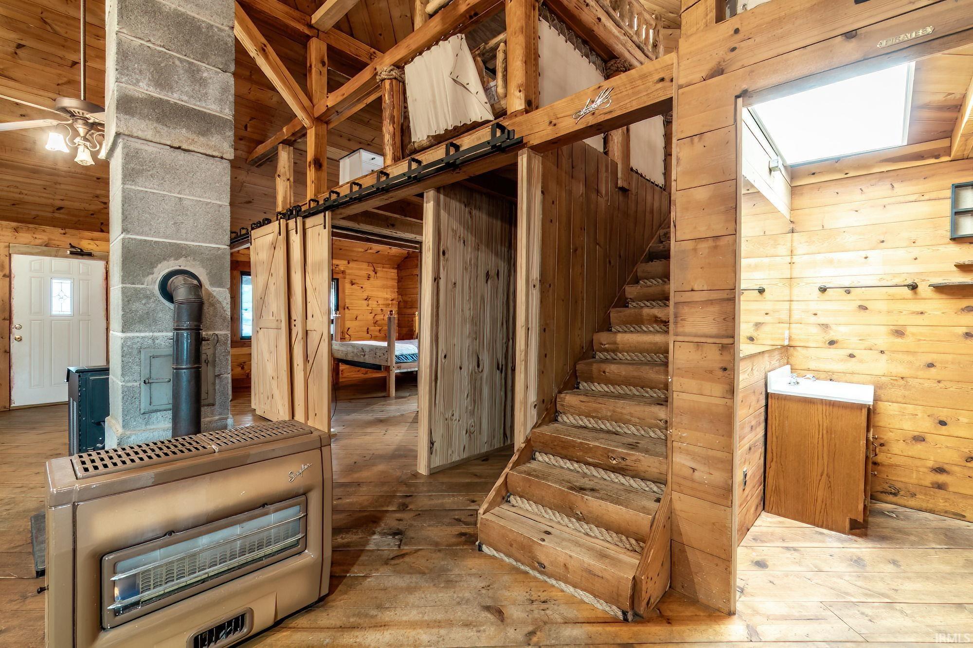 Stairs with wooden walls, a wood stove, hardwood / wood-style floors, and ceiling fan