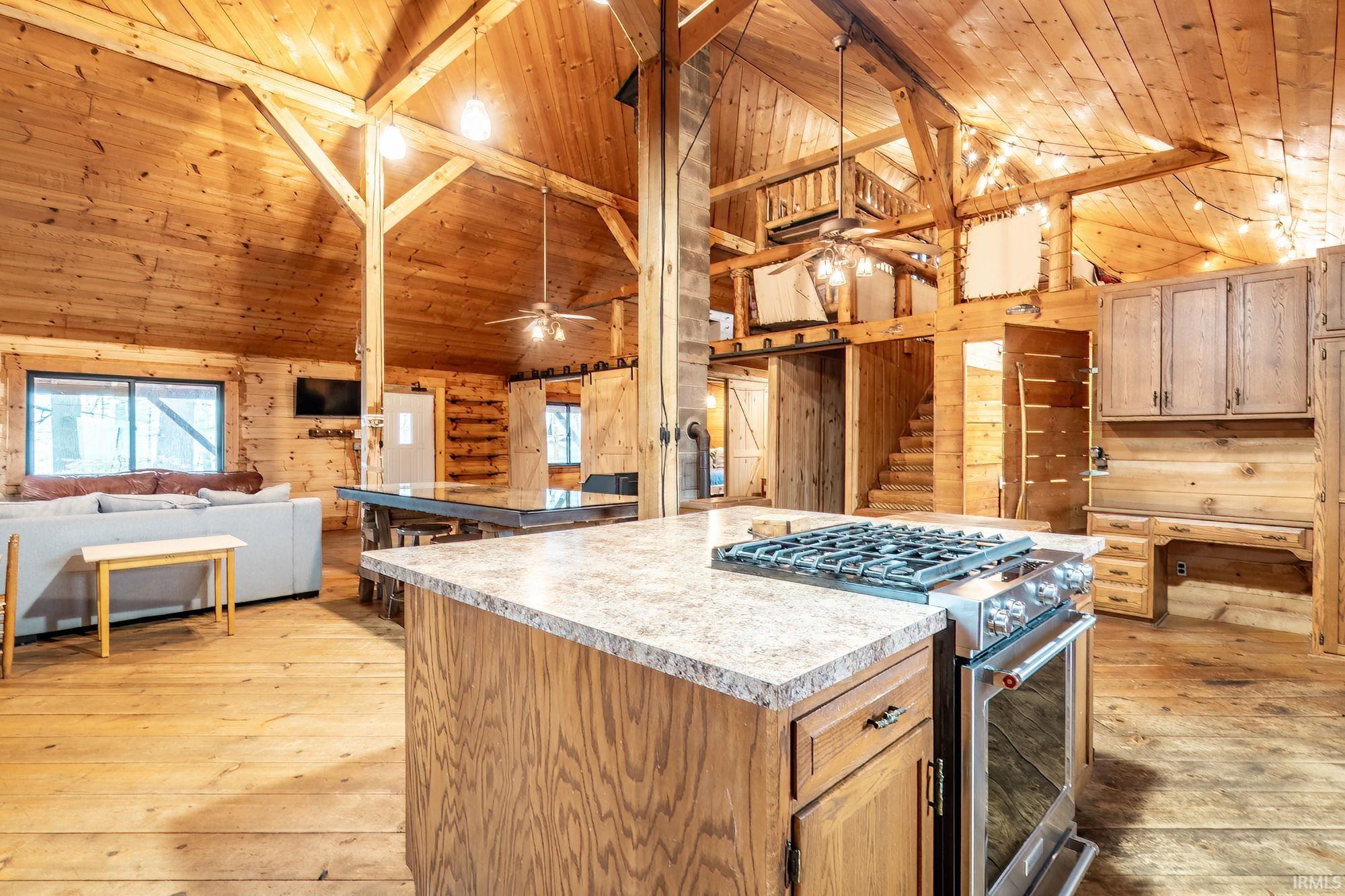 Kitchen with light wood-type flooring, a high wood beamed ceiling, stainless steel gas stove, wood walls, and open floor plan