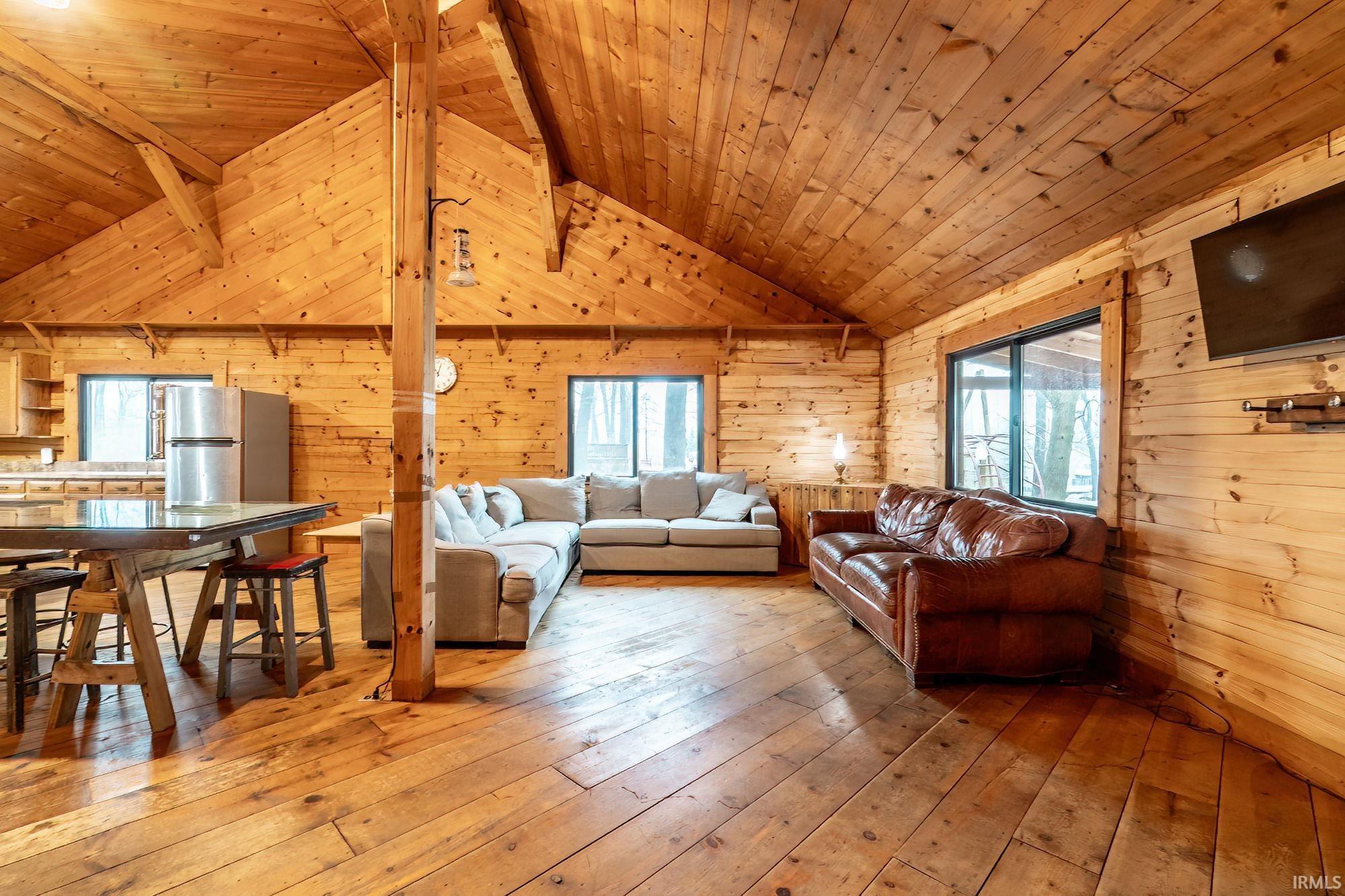 Living room with lofted ceiling with beams, wooden walls, wooden ceiling, and wood-type flooring